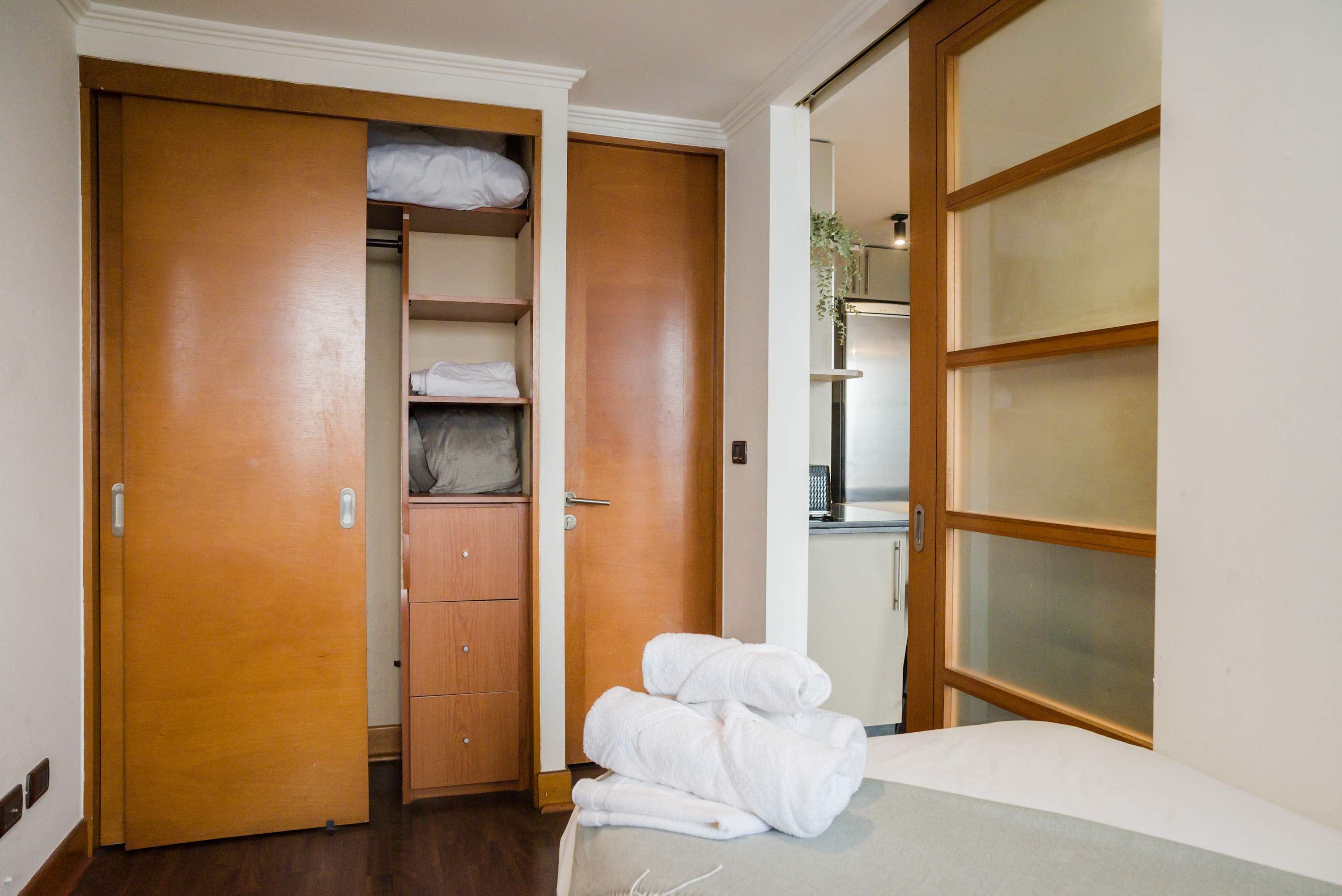 Cozy bedroom with ample storage and a glimpse into the modern kitchen, perfect for a comfortable stay.
