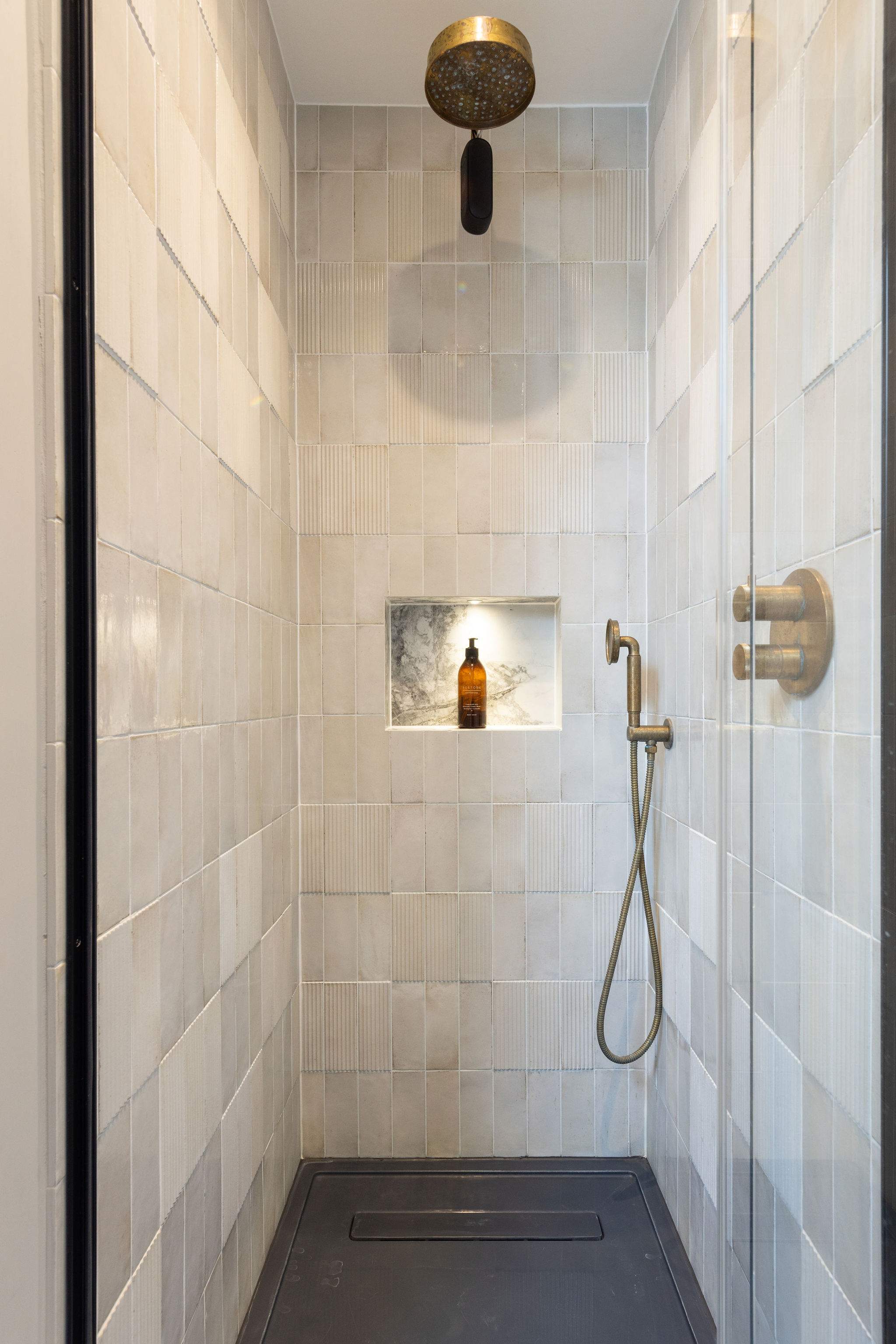 Stylish walk-in with brushed brass fixtures and a lit niche