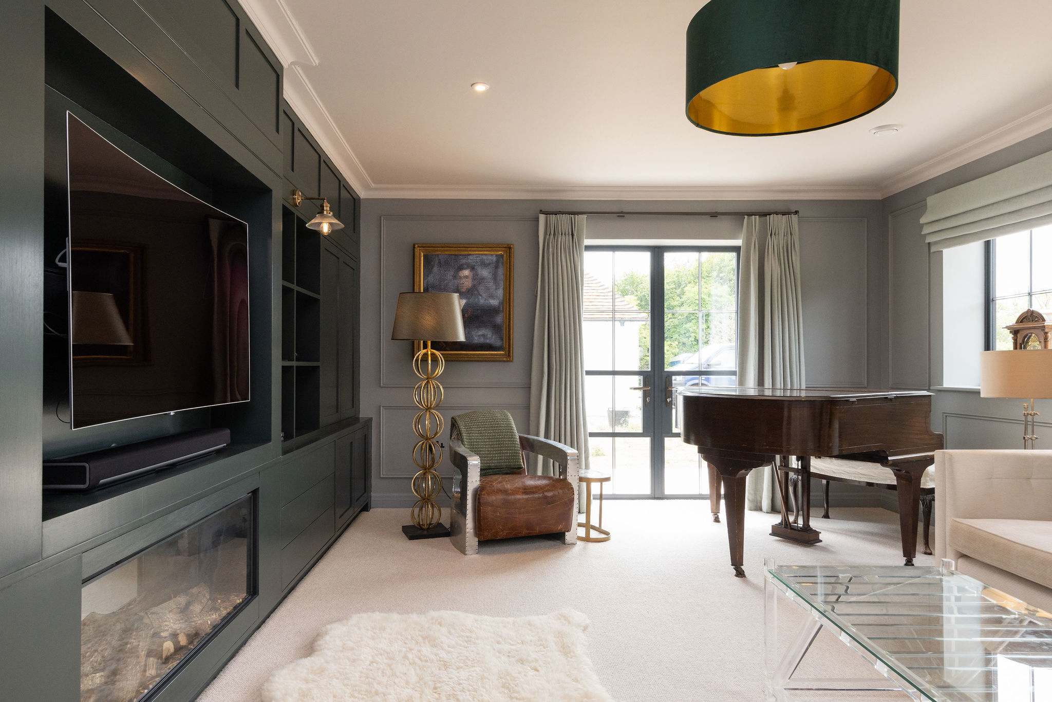 One of several elegant living spaces, featuring a grand piano, bespoke cabinetry, and garden views