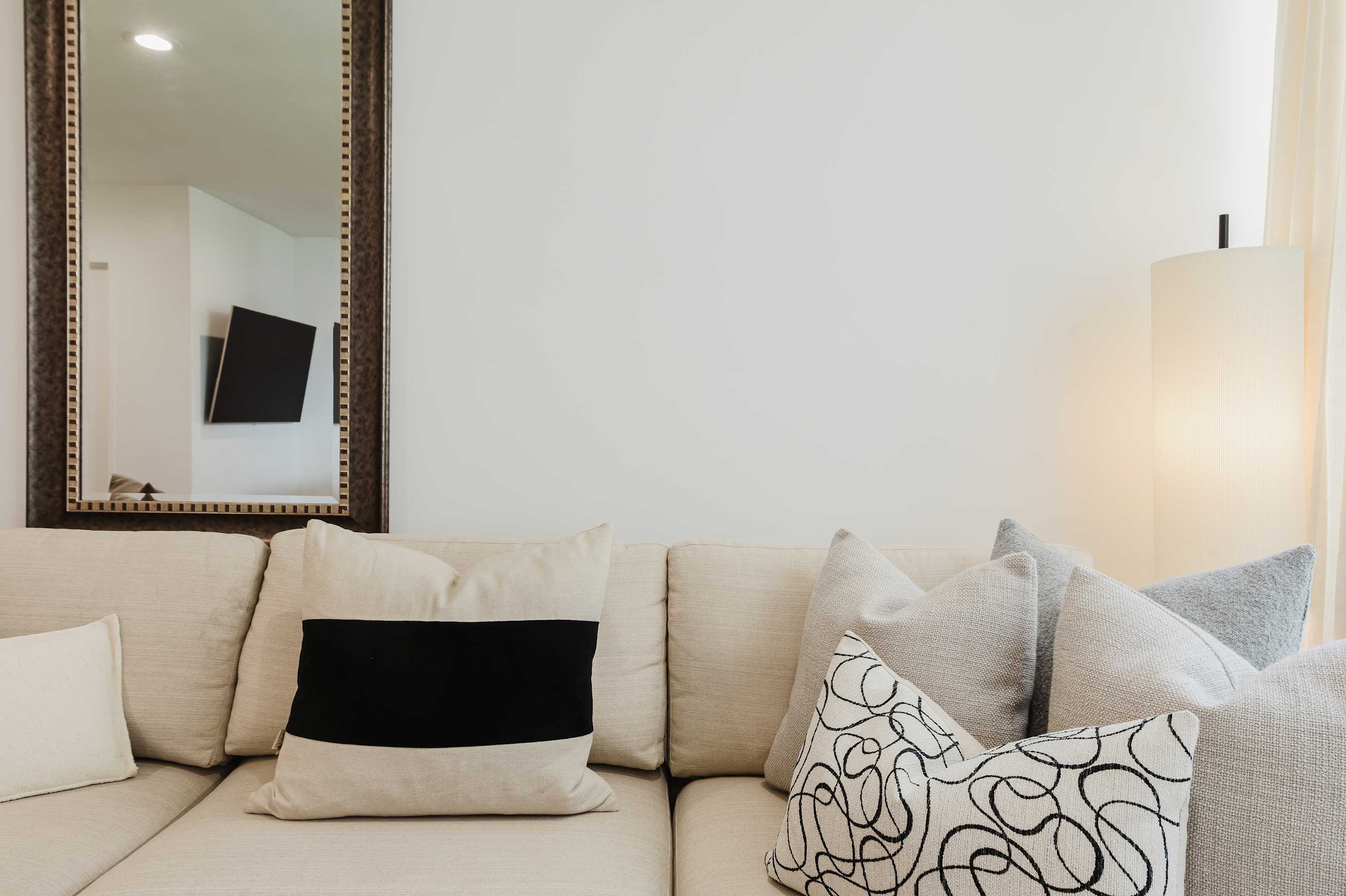 Living room seating area with a cream sofa, black-and-white throw pillows, and a full-length mirror.