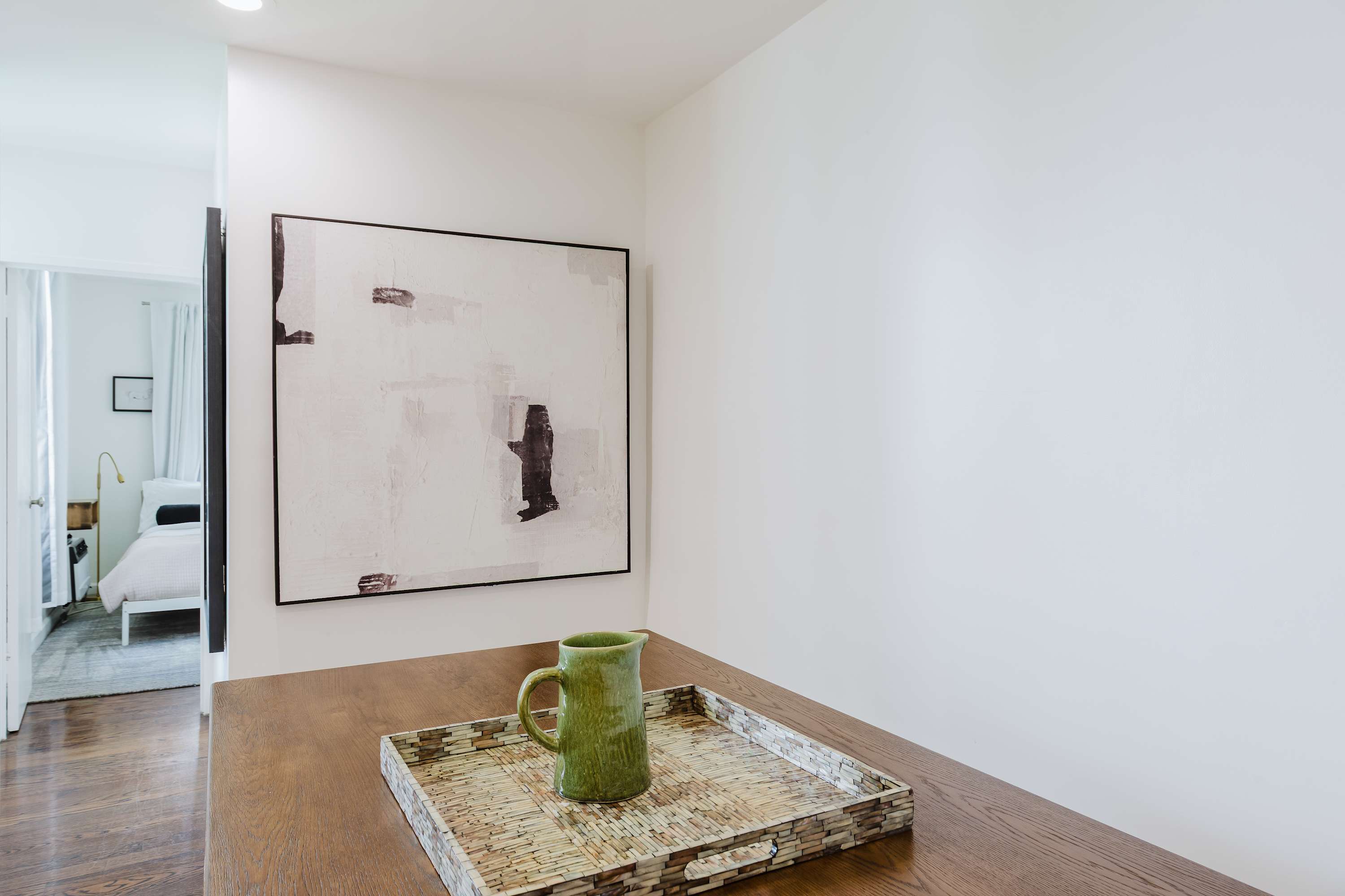 Dining table detail with a ceramic pitcher on a woven tray beneath abstract artwork.