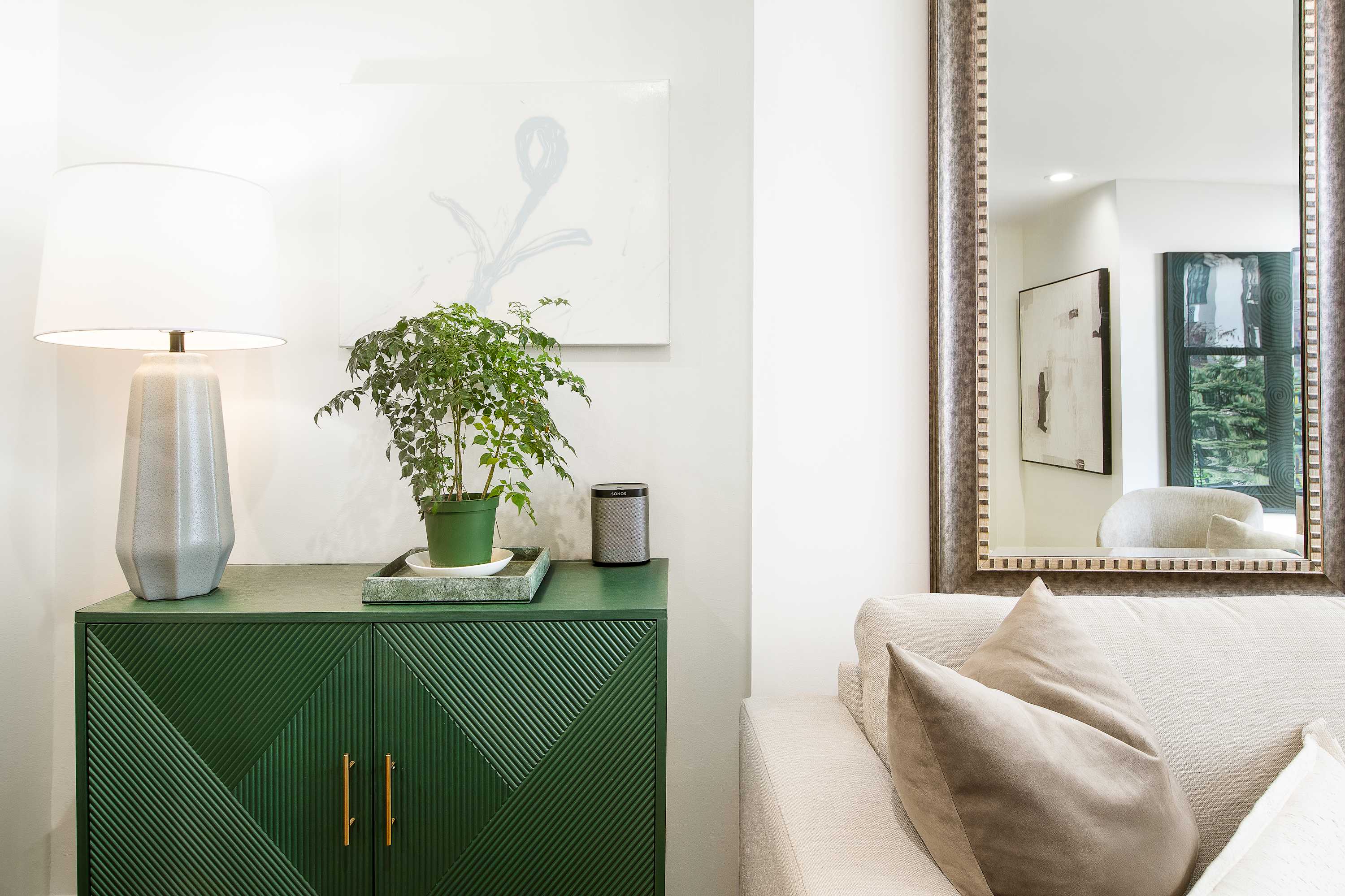 Living room corner with a green lacquered cabinet, table lamp, and potted plant beside the sofa.