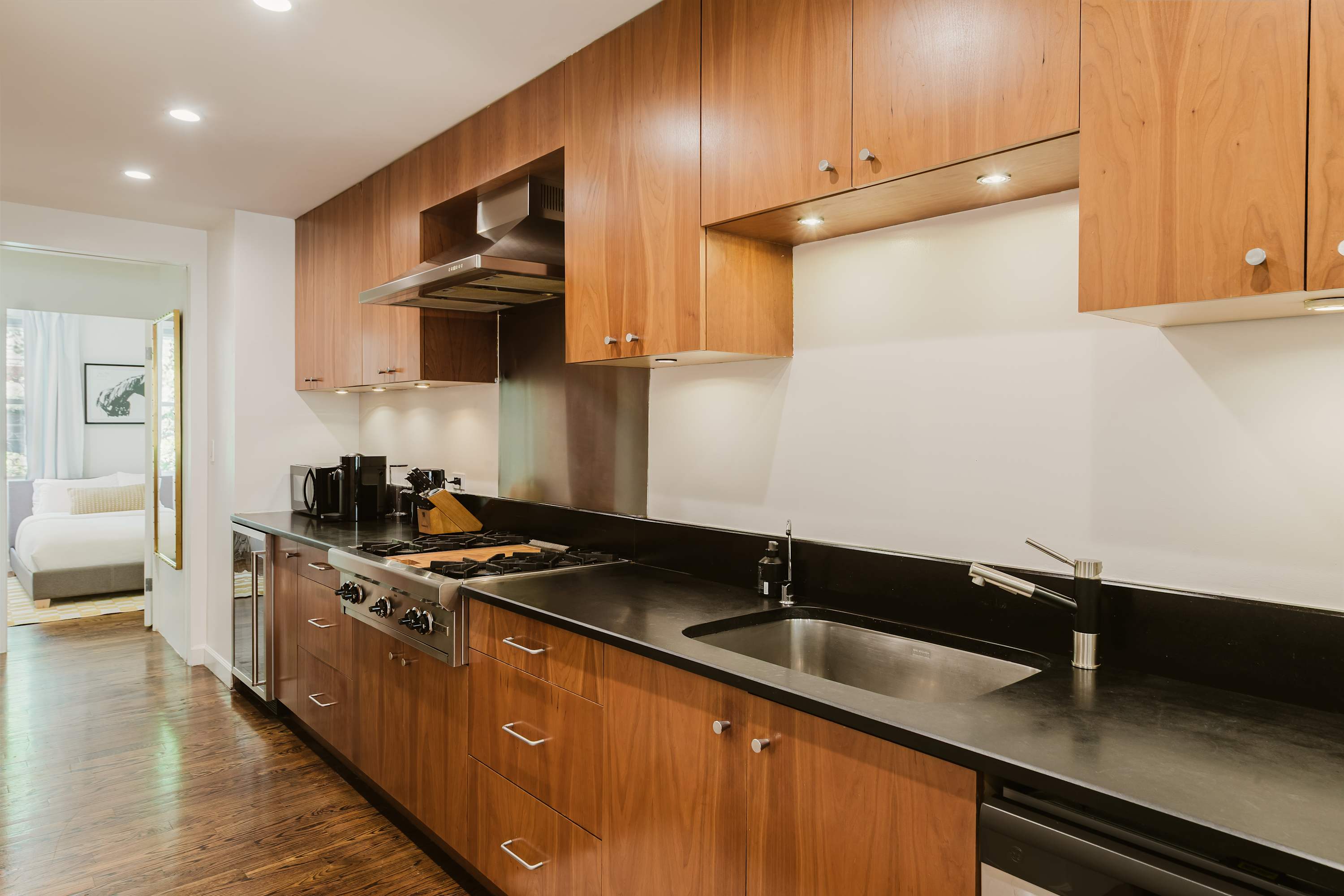 Galley kitchen with wood cabinetry, black countertops, stainless range, and pendant lighting.