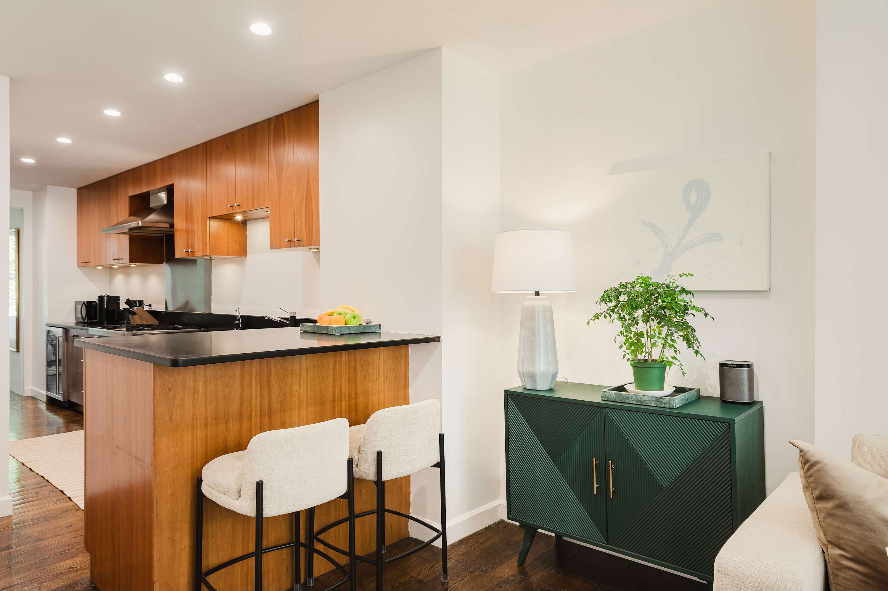 Wood-cabinet kitchen with a black countertop, breakfast bar, and stools, open to the living room.