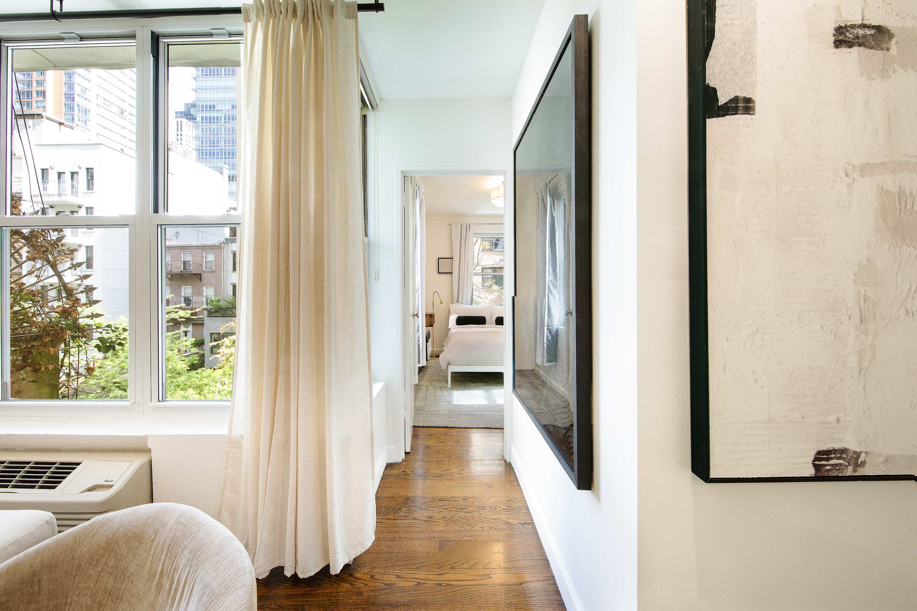 Hallway view toward a bedroom, with a wall-mounted TV, tall window, and city view.