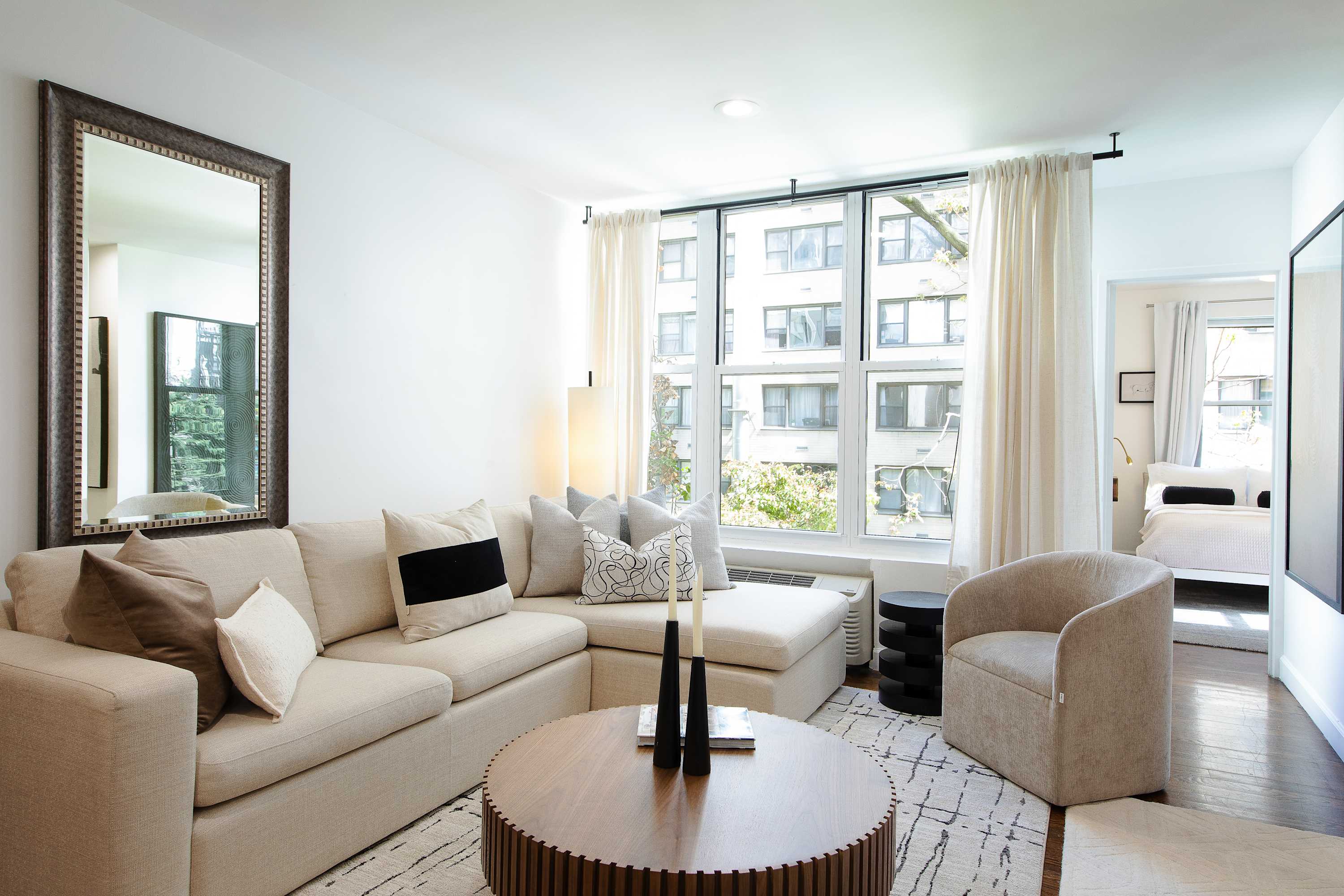 Living room with an L-shaped cream sectional, round wood coffee table, and city-view windows.
