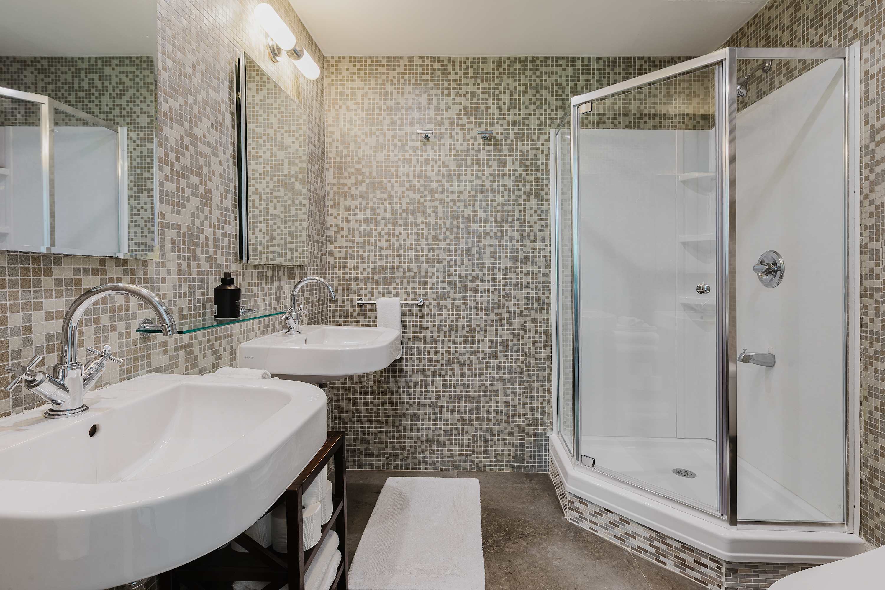 Bathroom with a mosaic-tiled glass shower, double wall-mounted sinks, and a vanity mirror.