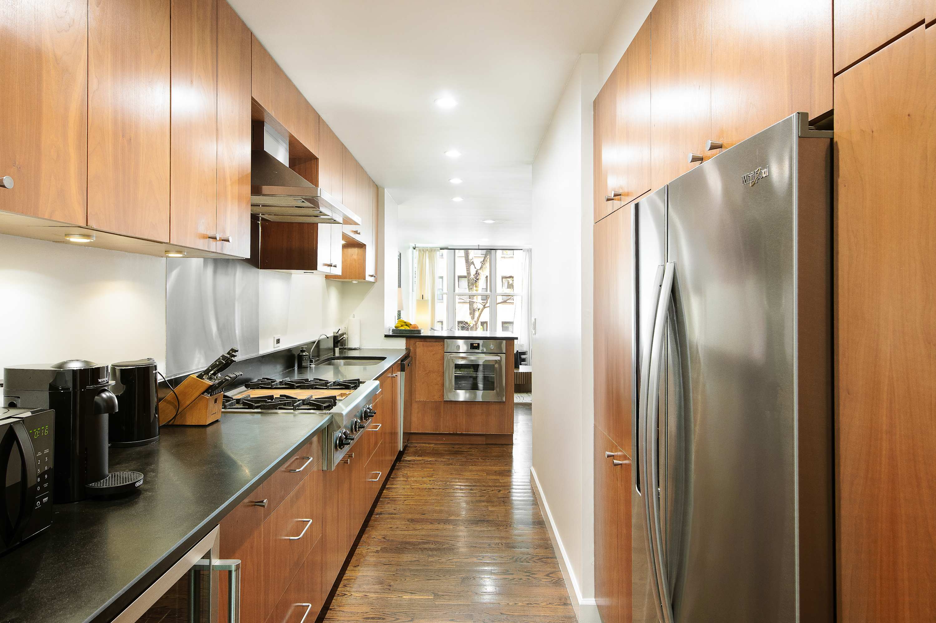 Galley kitchen view toward the hallway, with wood cabinetry and a stainless refrigerator.