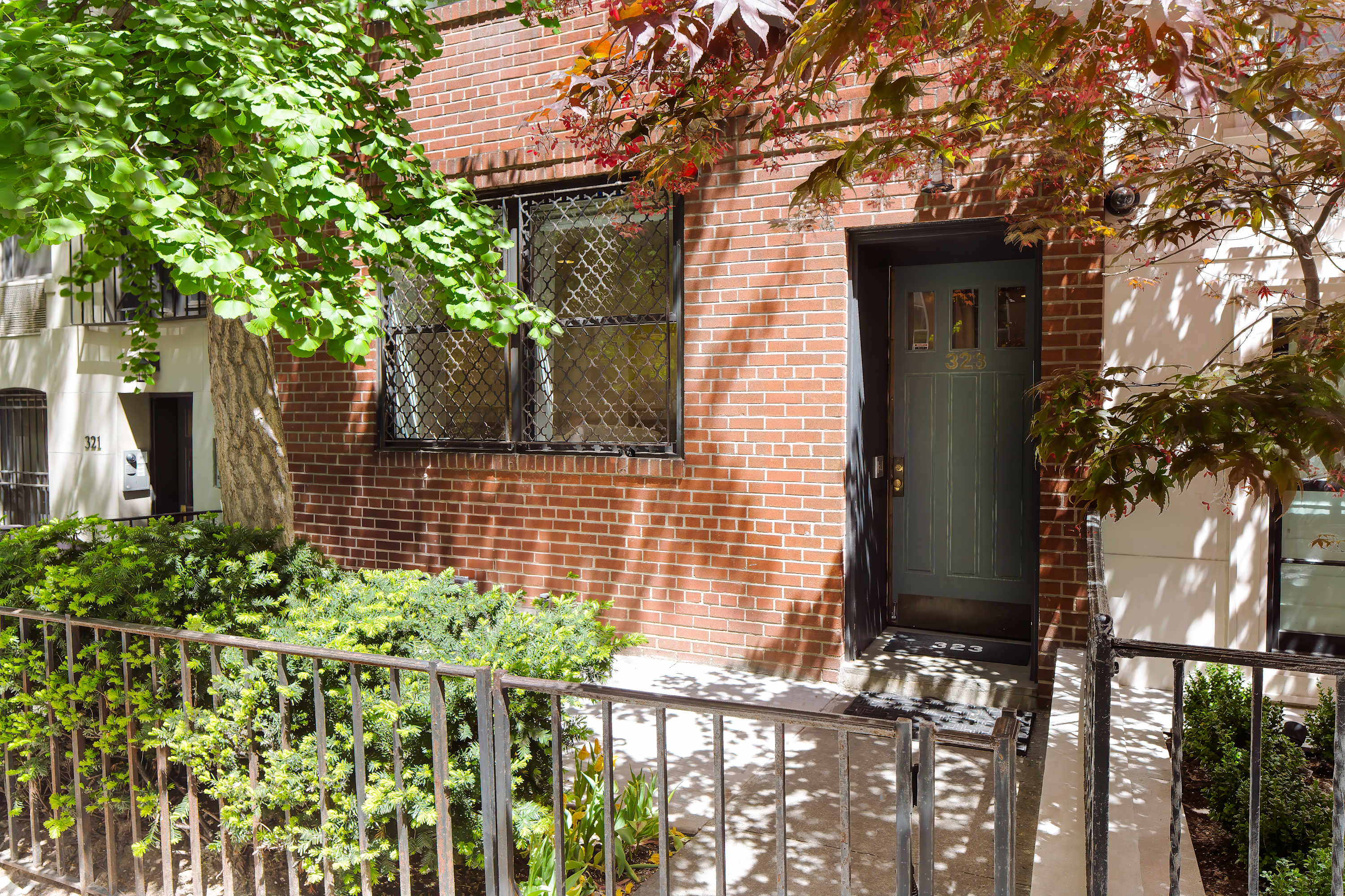 Entrance to the brick townhouse with a paneled wood door, iron railing, and landscaping.