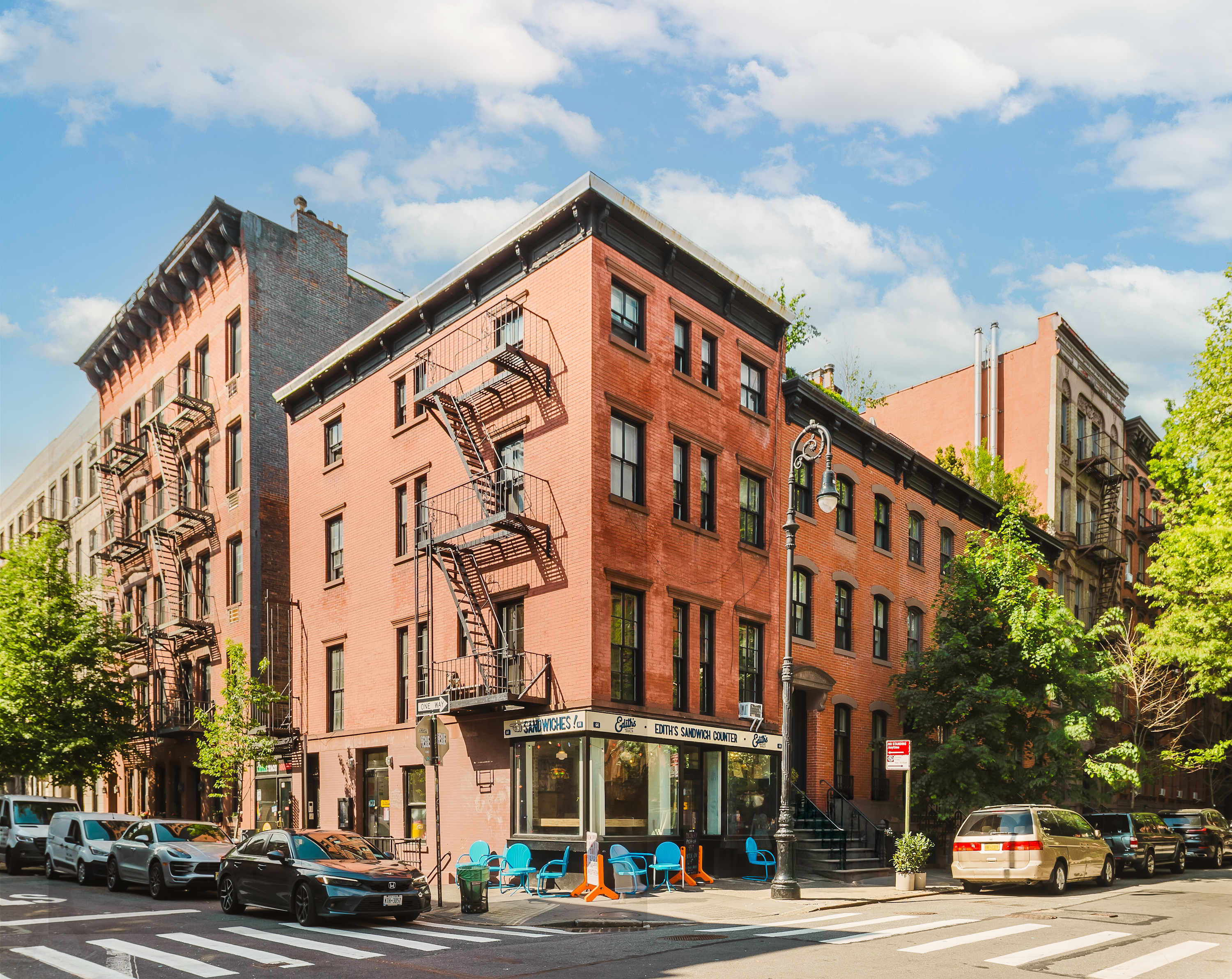 Exterior street view of the red-brick West Village corner building with cast-iron fire escapes and a tree-lined sidewalk.