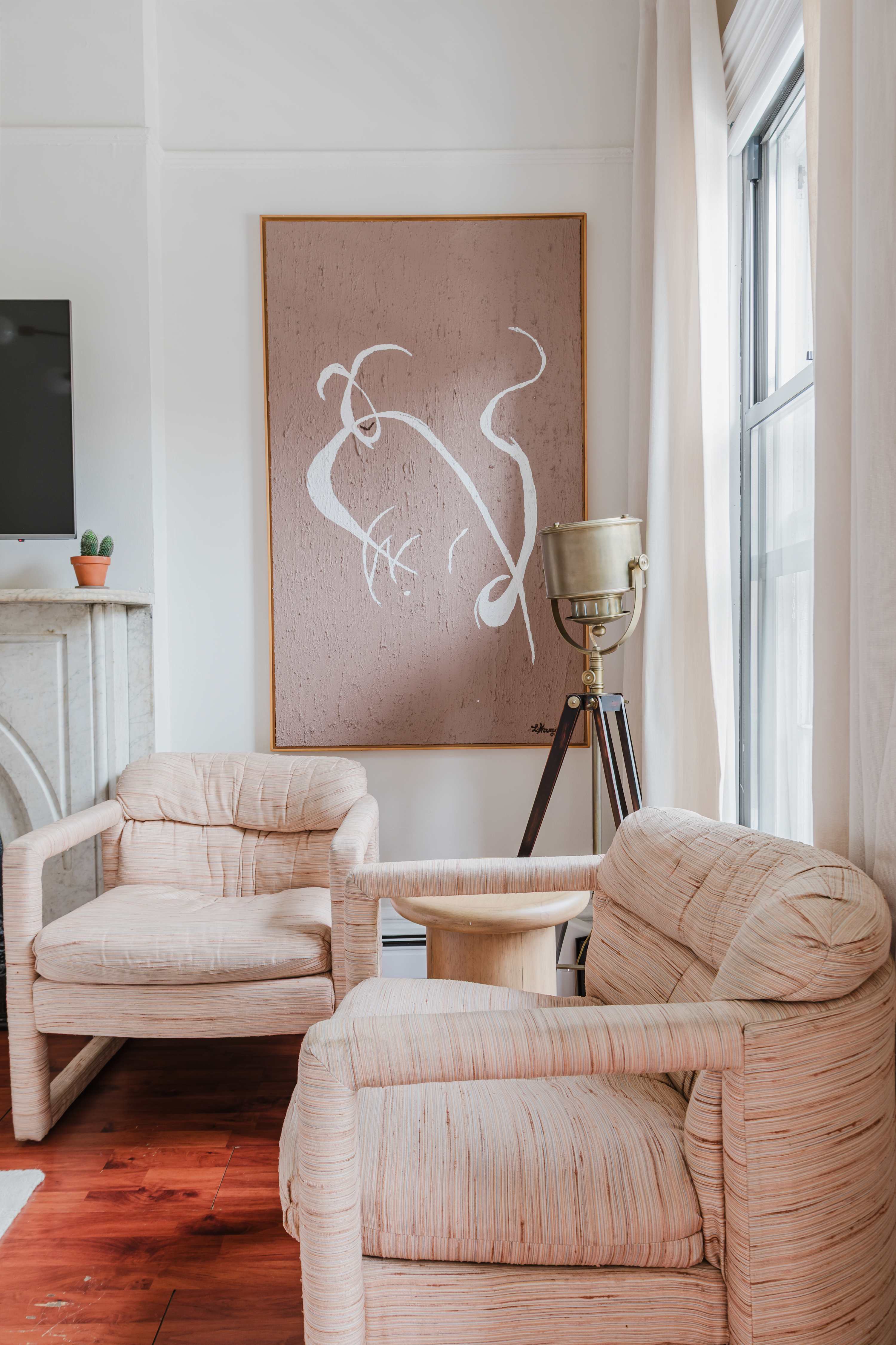 Seating nook with two blush pink armchairs, a marble fireplace, wall-mounted TV, and a large abstract pink artwork.