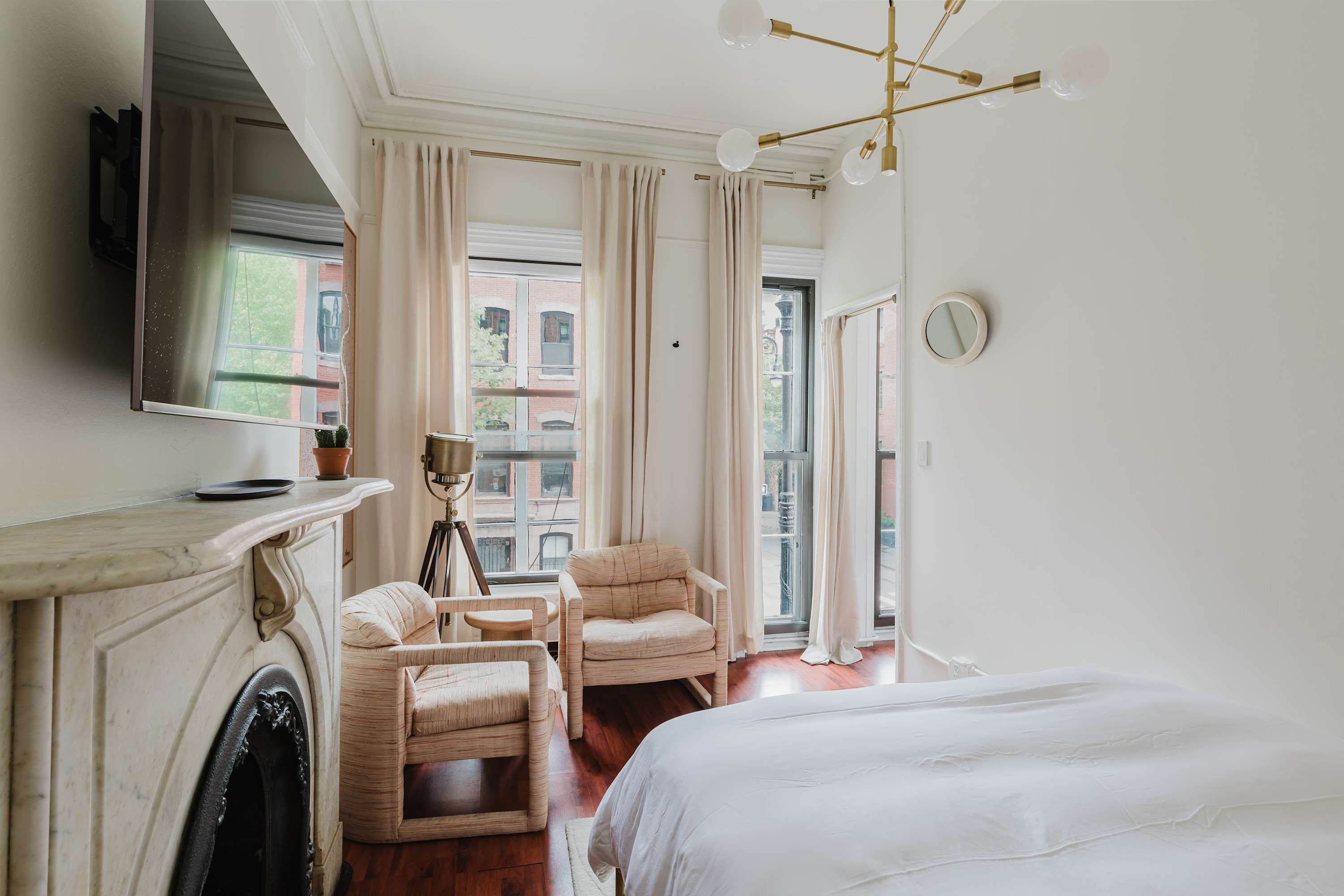 Bedroom corner with a marble fireplace, wall-mounted TV, two upholstered armchairs, and a bay window overlooking the street.