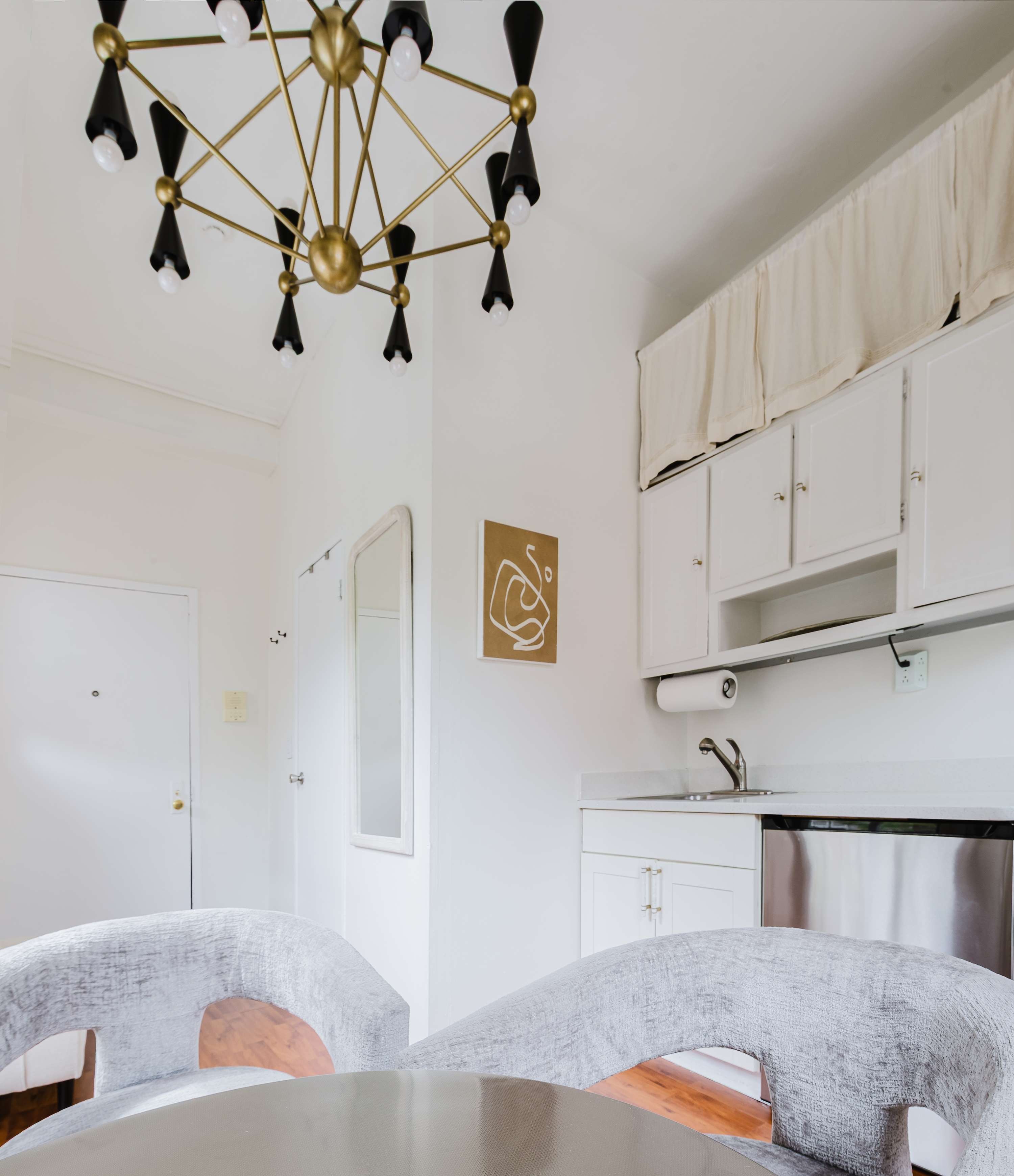 Kitchen and dining nook with a brass sputnik chandelier, curved gray velvet chairs, white cabinetry, and stainless appliances.
