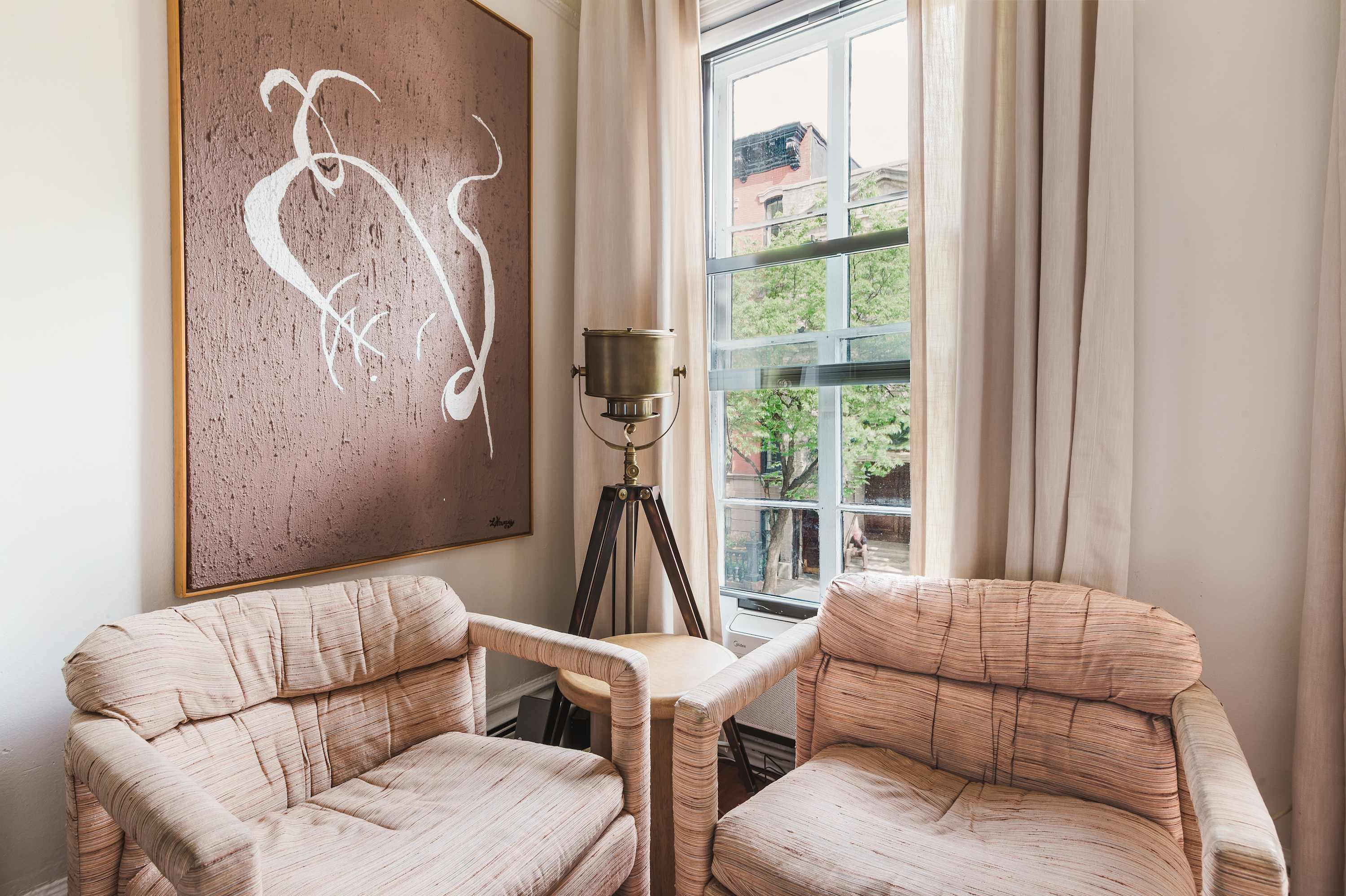 Window seating nook with two blush pink armchairs beneath the abstract pink artwork, overlooking the street.