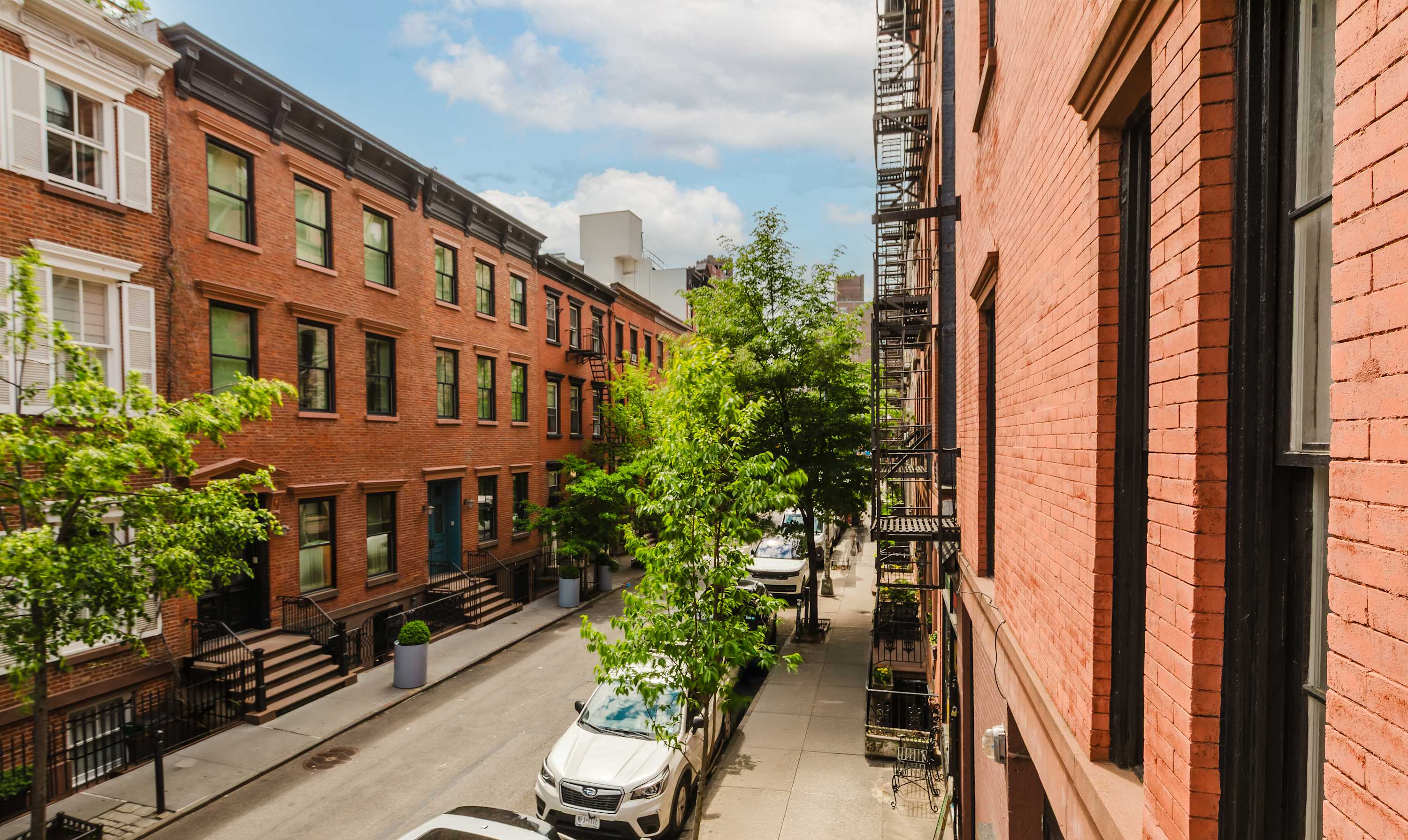 Tree-lined West Village street with rows of red-brick townhouses and fire escapes.