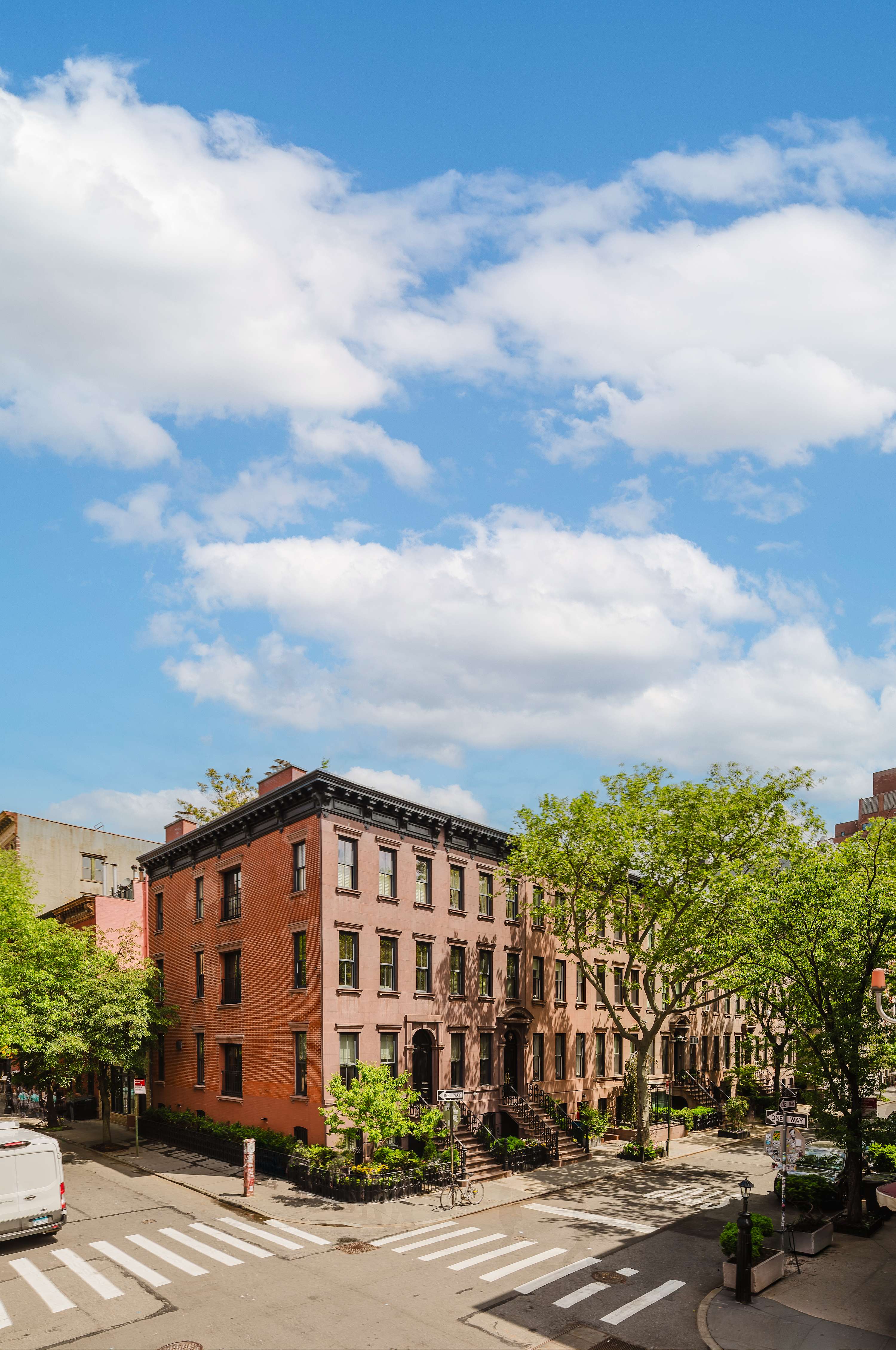 Sunlit West Village street corner with brick townhouses and street trees.