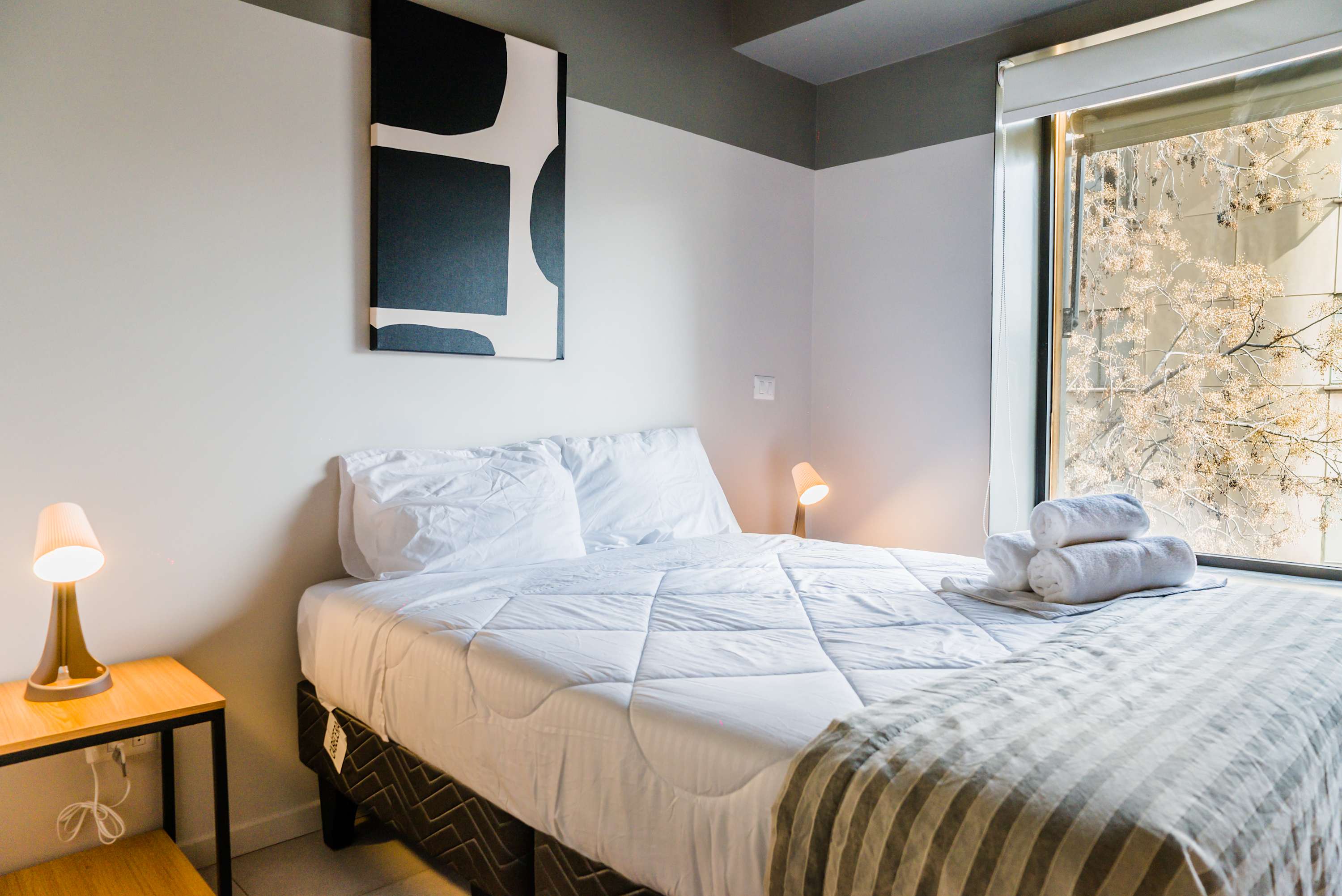 Relax in this cozy bedroom with modern decor and natural light, perfect for a restful stay in the heart of the city.
