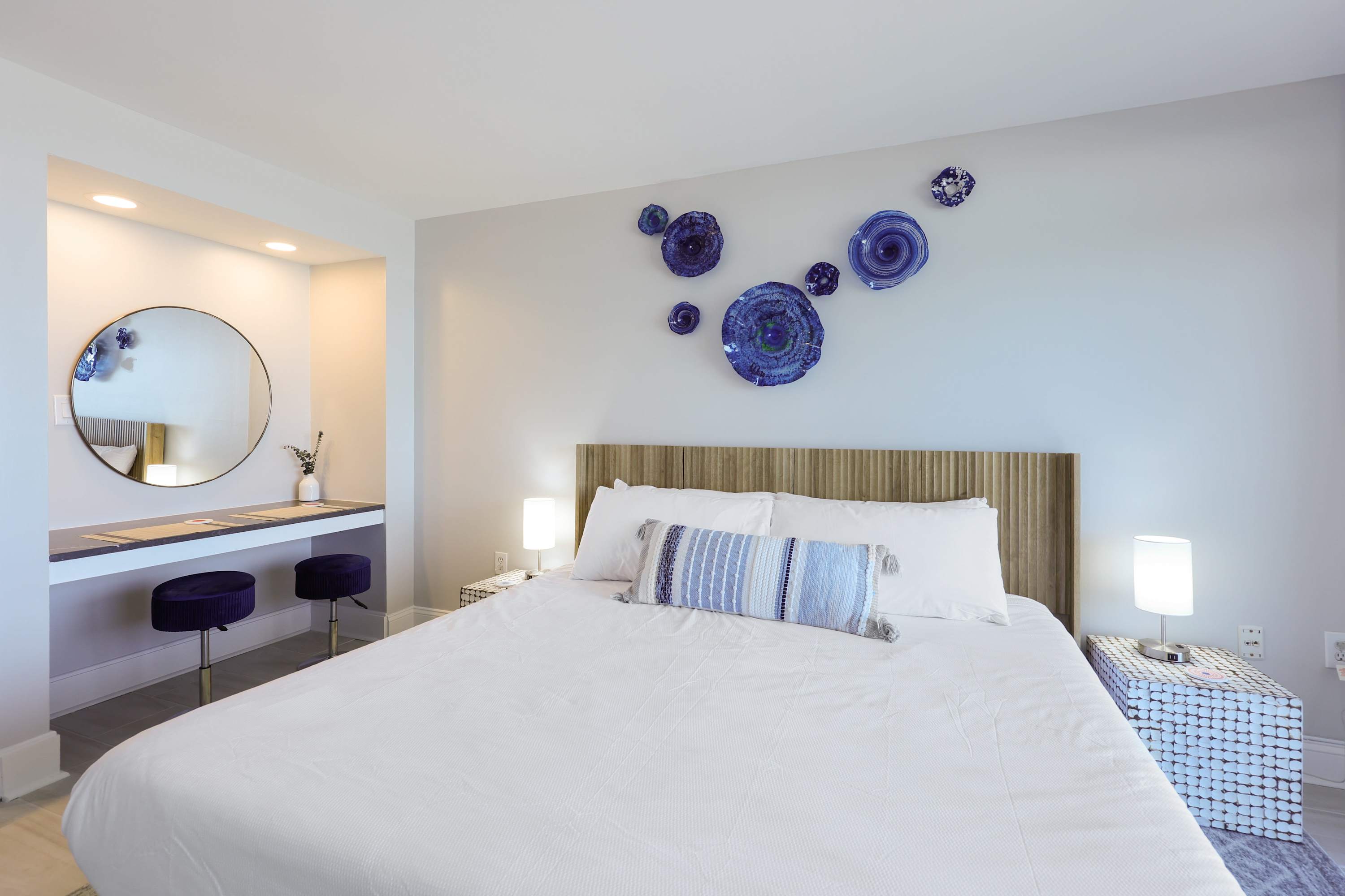 Drift off in this dreamy coastal bedroom featuring bold blue art, a plush king bed, and a stylish vanity nook—perfect for relaxing after a day at the beach. Coastal comfort meets modern charm in every detail.