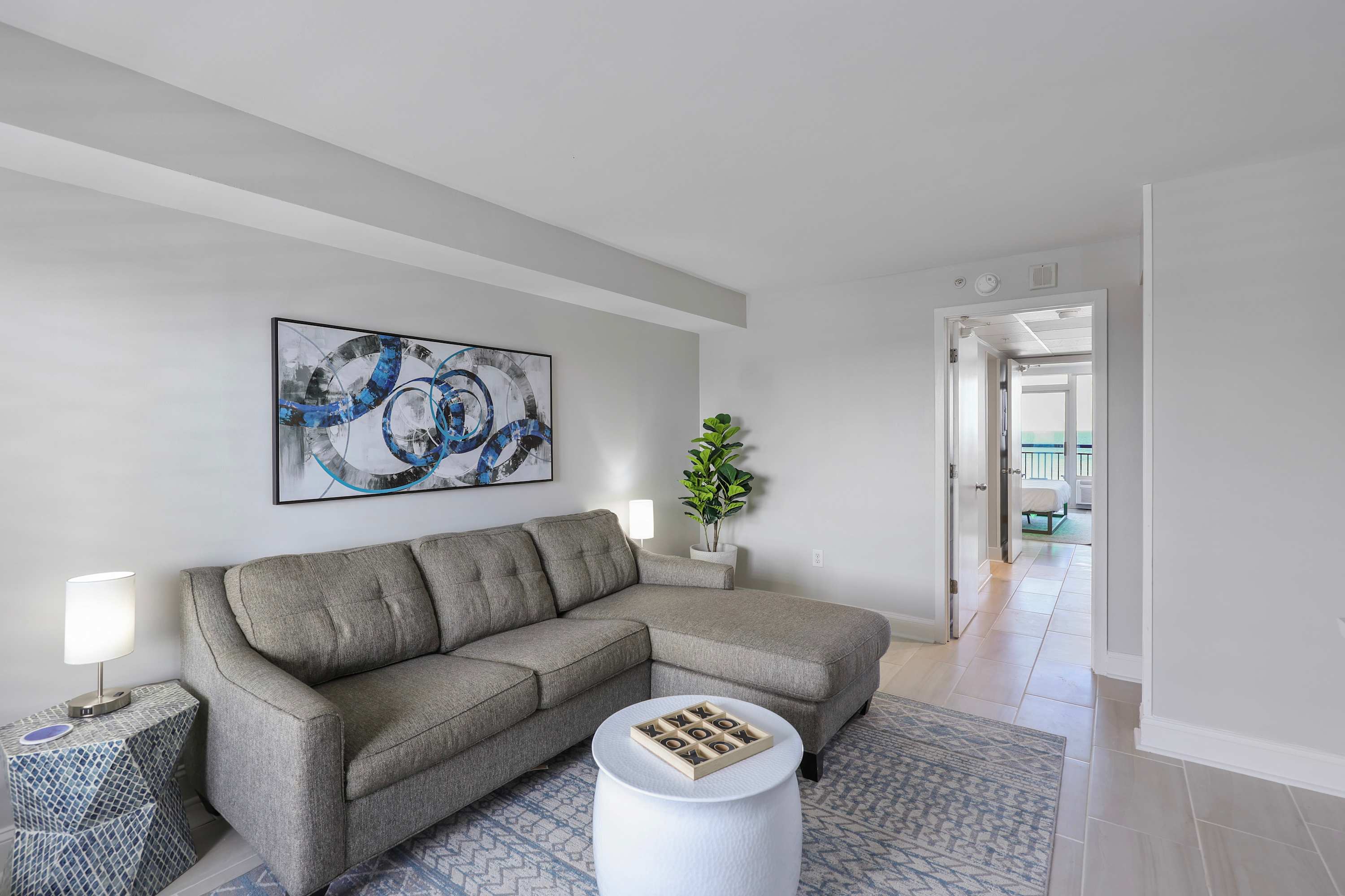 Cozy up in this chic coastal living space featuring a comfy sectional, playful decor, and a peek into your ocean-view bedroom—perfect for relaxing after a beach day or enjoying a game night in.