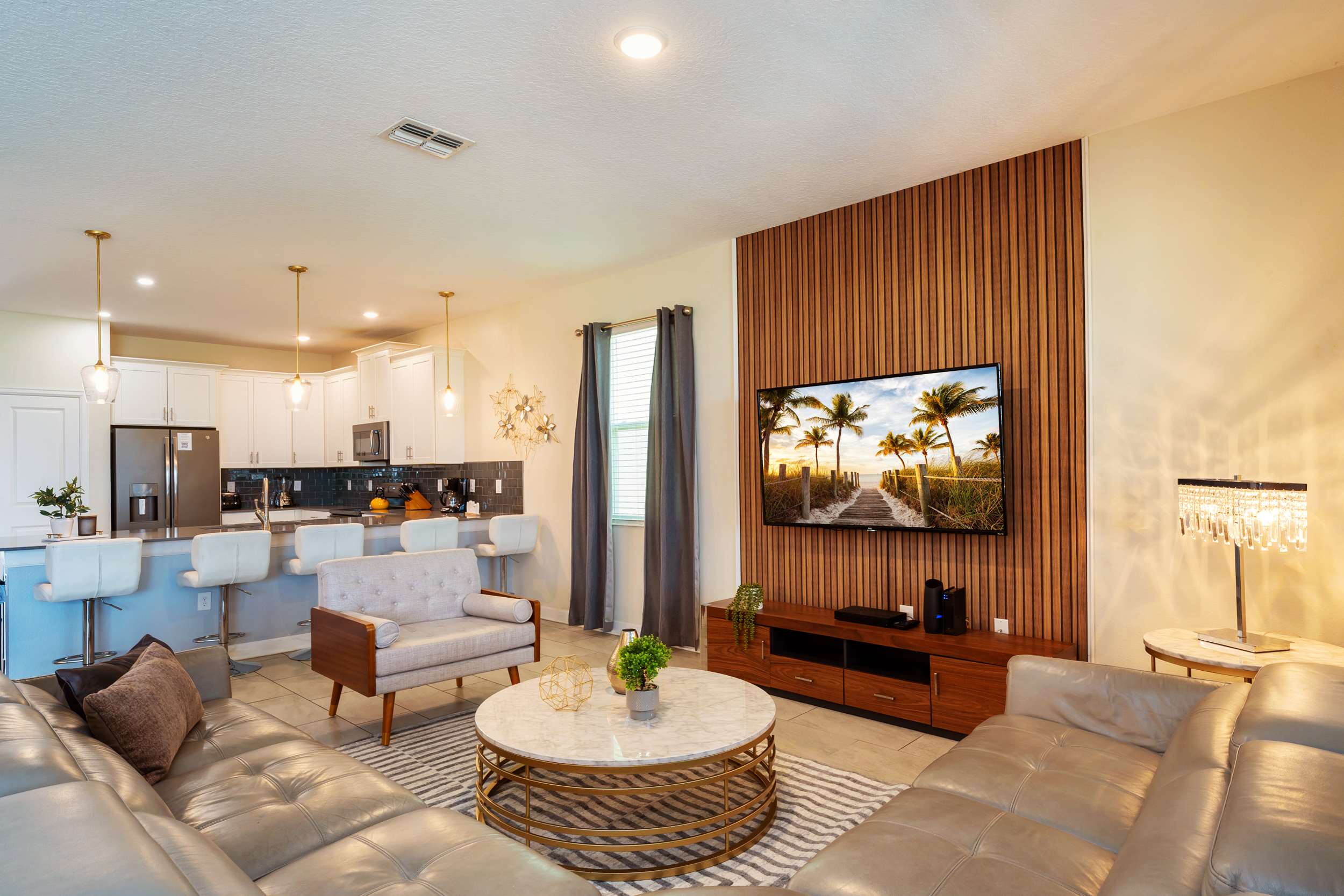 Open-plan living room with leather seating, a marble coffee table, and a large TV framed by a dramatic wood-slat accent wall beside the fully equipped kitchen.