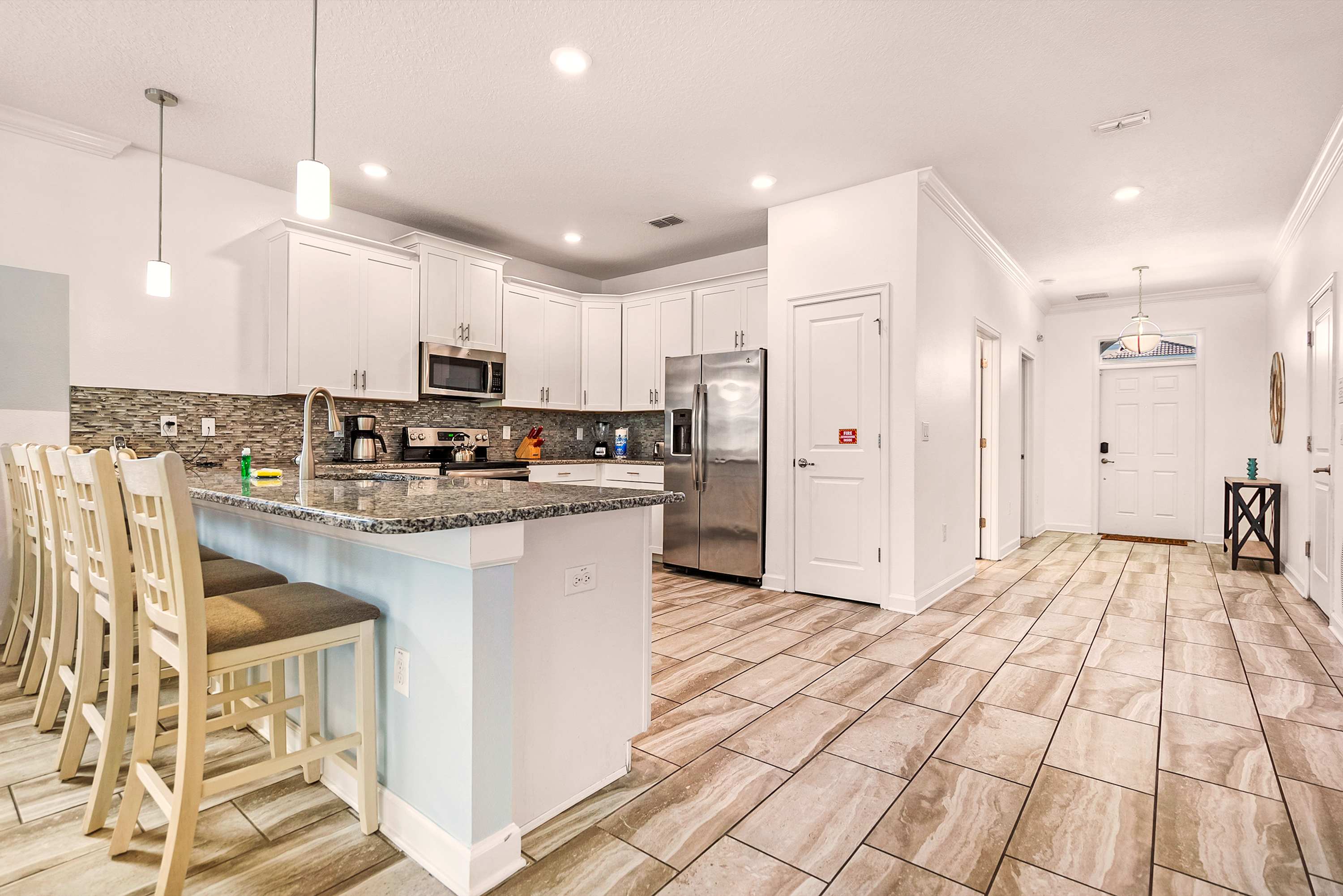 Private kitchen with granite peninsula seating for six, white cabinetry, stainless-steel appliances, and a textured gray backsplash for effortless group meal preparation.