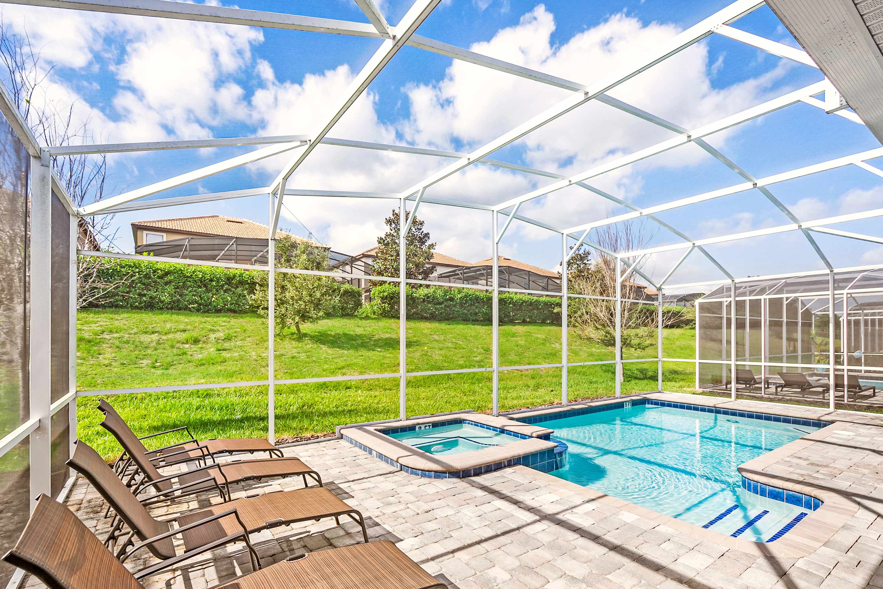 Relax in your private screened-in pool and hot tub, surrounded by lush greenery and ample lounge seating, perfect for unwinding under the blue sky.