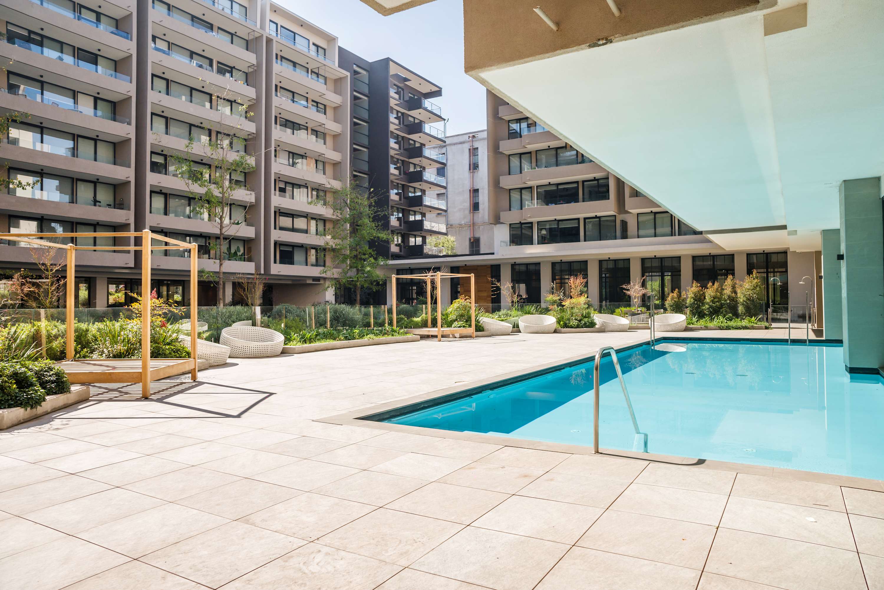 Relax by the pristine pool surrounded by lush greenery and modern architecture, offering a perfect urban retreat.