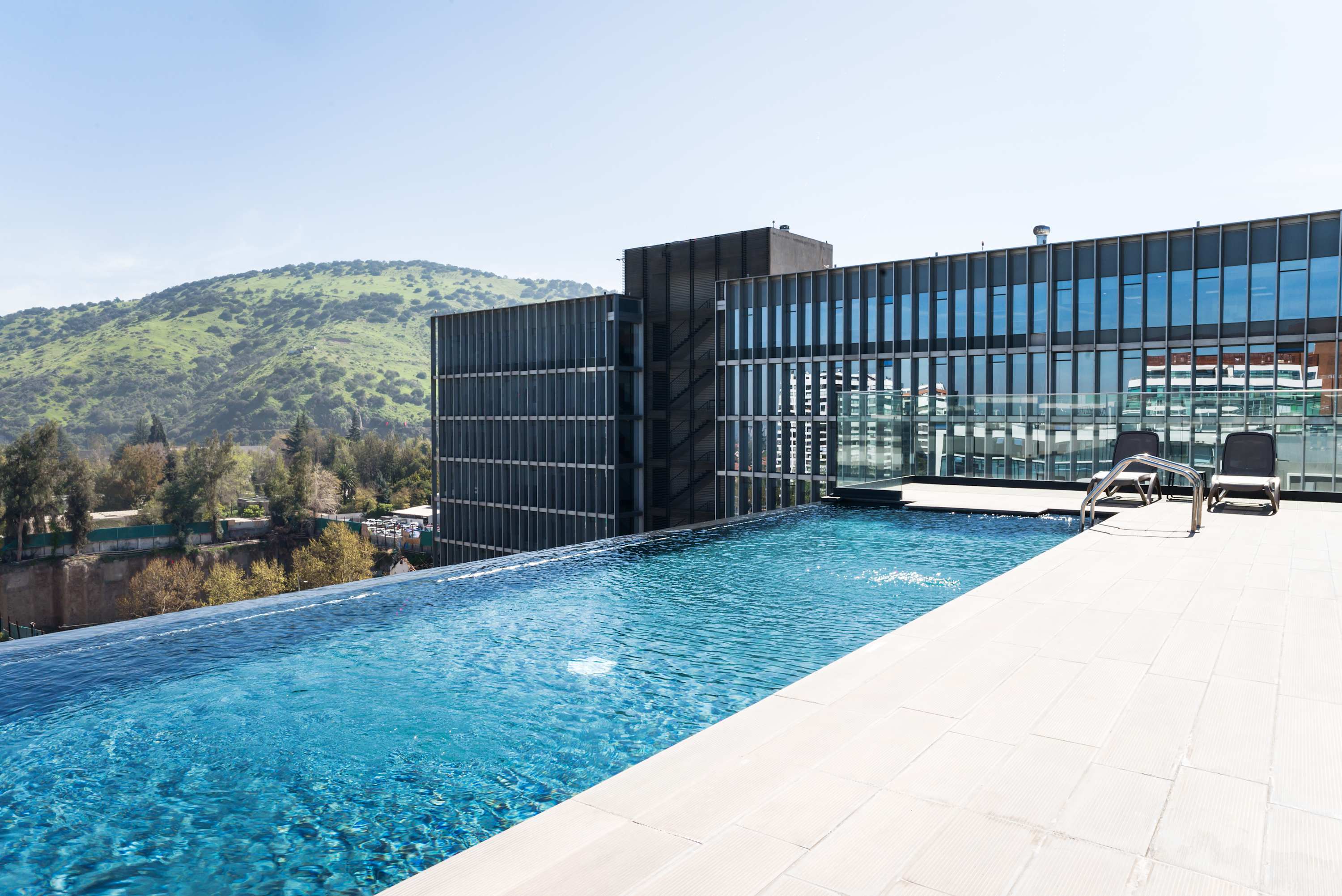Enjoy a refreshing dip in the rooftop infinity pool with stunning views of lush hills and modern architecture.