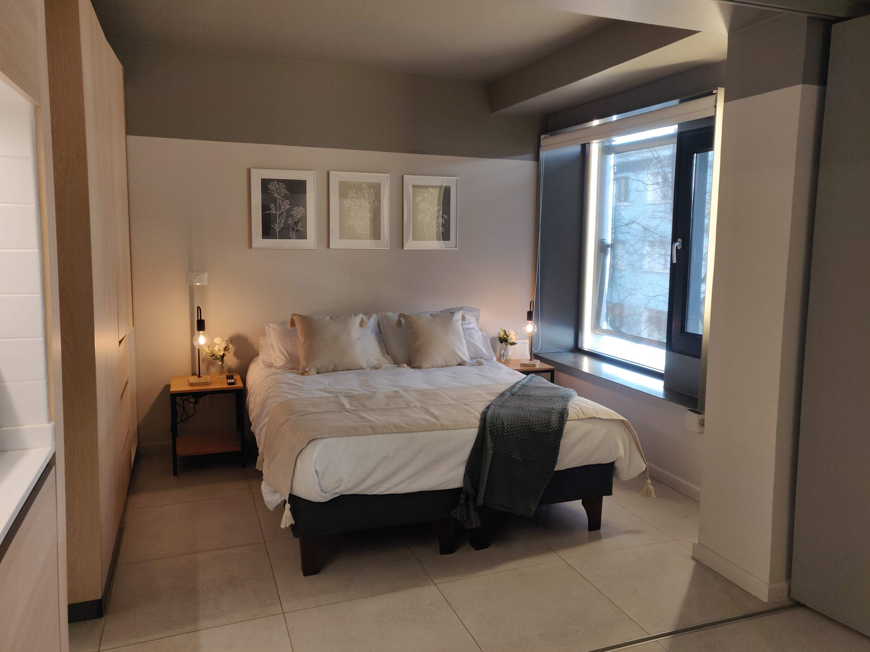 Relax in this cozy bedroom with modern decor and ample natural light, perfect for a restful stay.