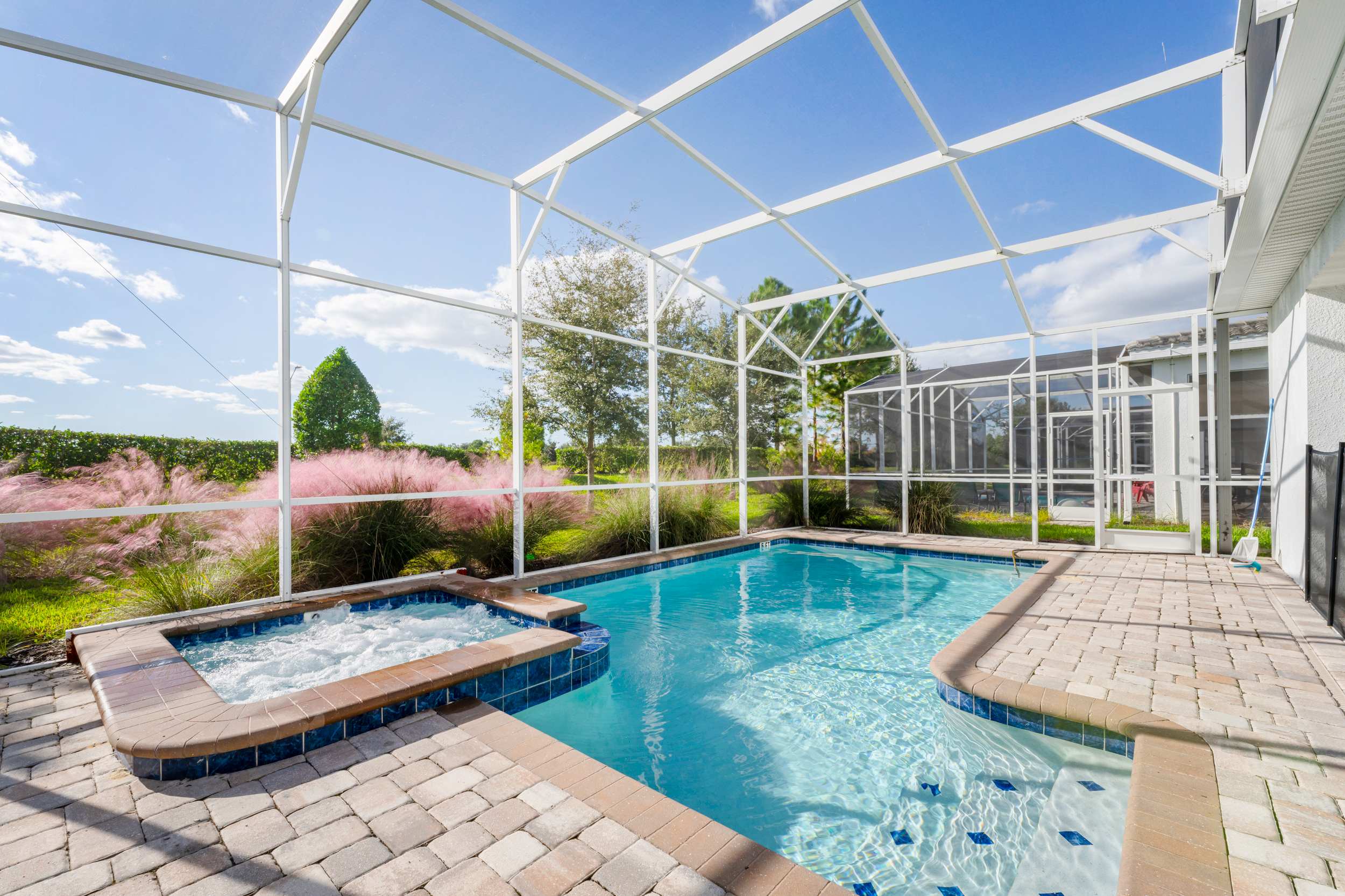 Relax in your private screened-in pool and hot tub oasis, surrounded by lush greenery and under a clear blue sky.