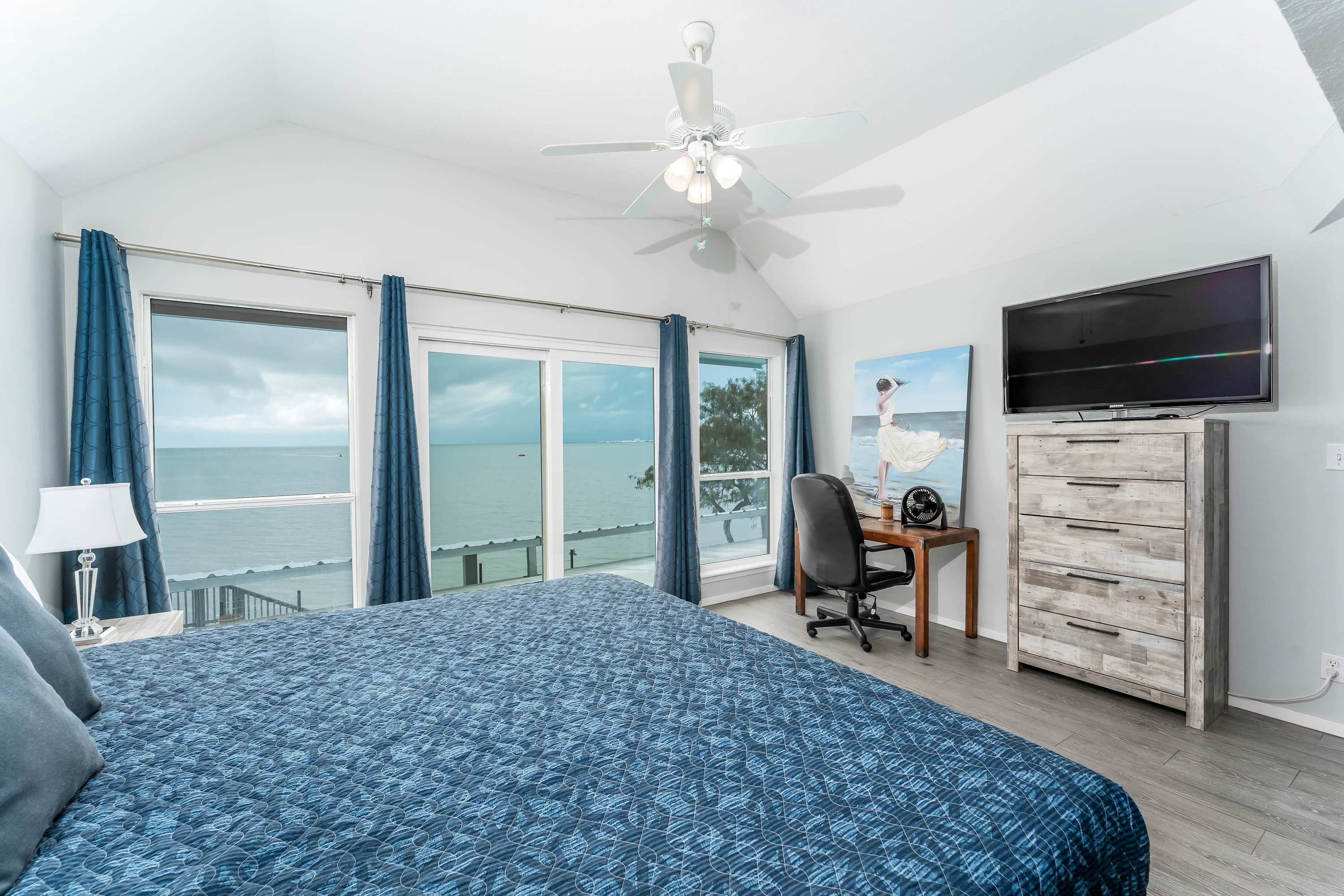 Primary Bedroom with King Bed & Ensuite — Spacious upstairs retreat with king bed, TV, and floor-to-ceiling water views. Ensuite bathroom includes shower and vanity.