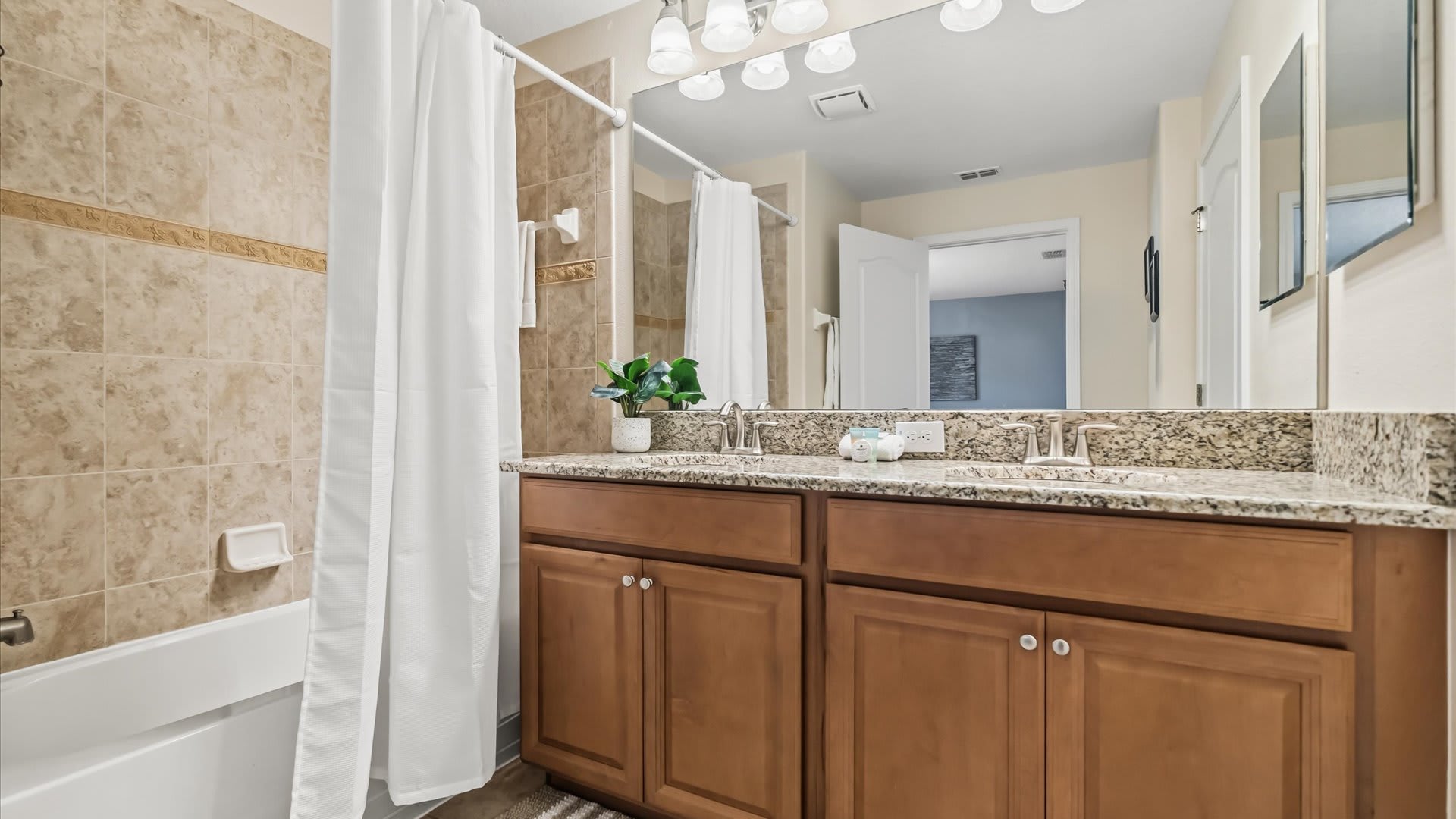 En-suite bathroom with dual sinks, granite countertops, and a bathtub and shower combo.