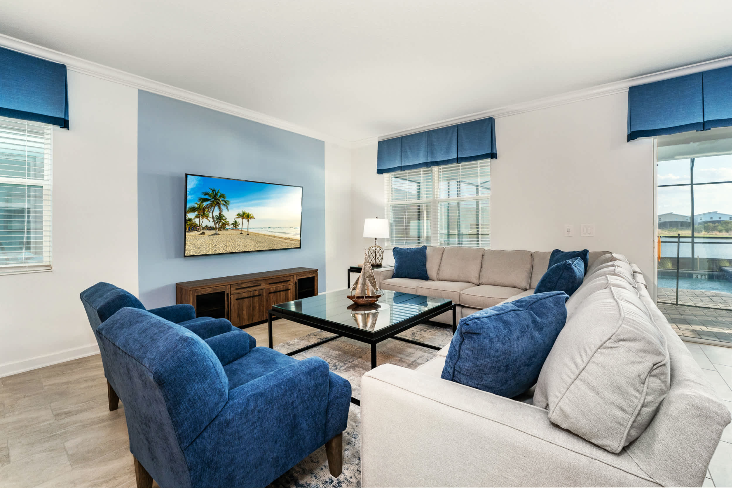 Relax in this spacious living room with plush seating, a large TV, and abundant natural light, perfect for family gatherings.
