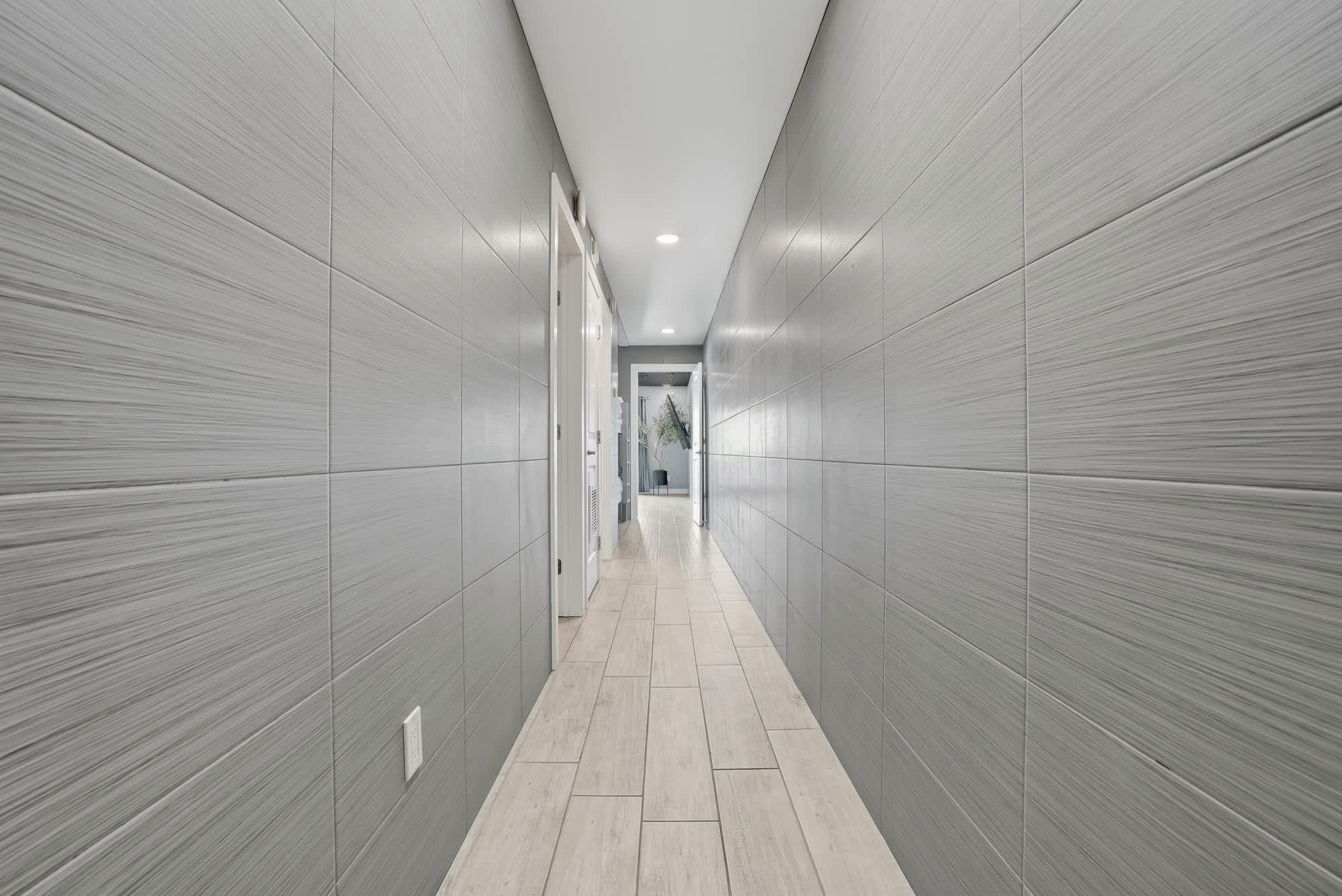 The Summit 1217 – Long hallway with gray textured walls and tile flooring, leading to a door at the end.