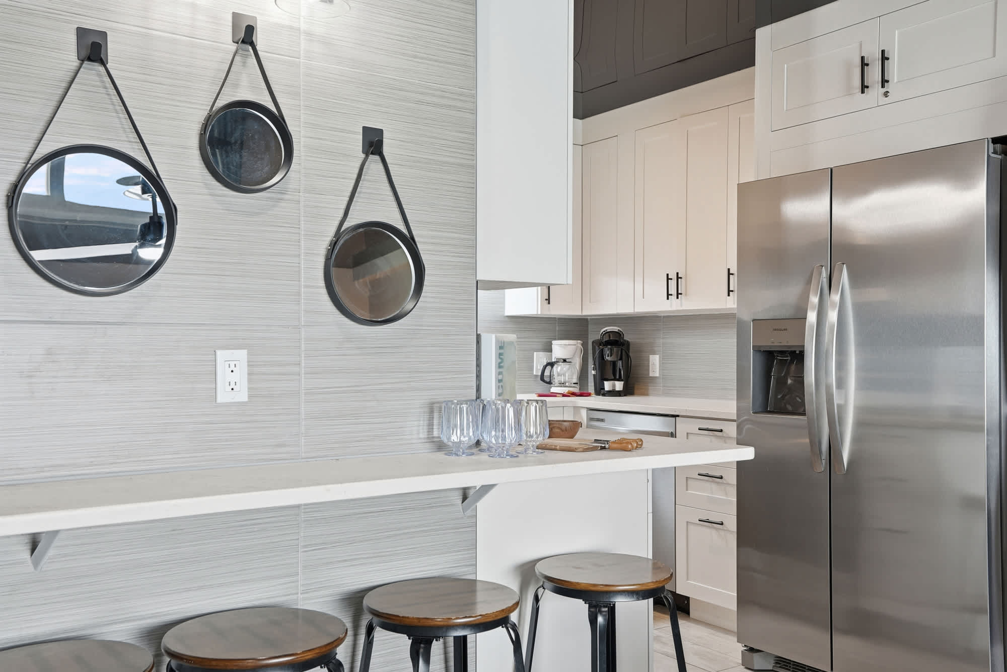 The Summit 1217 – Modern kitchen with bar stools, stainless steel refrigerator, mirrors, and coffee maker.