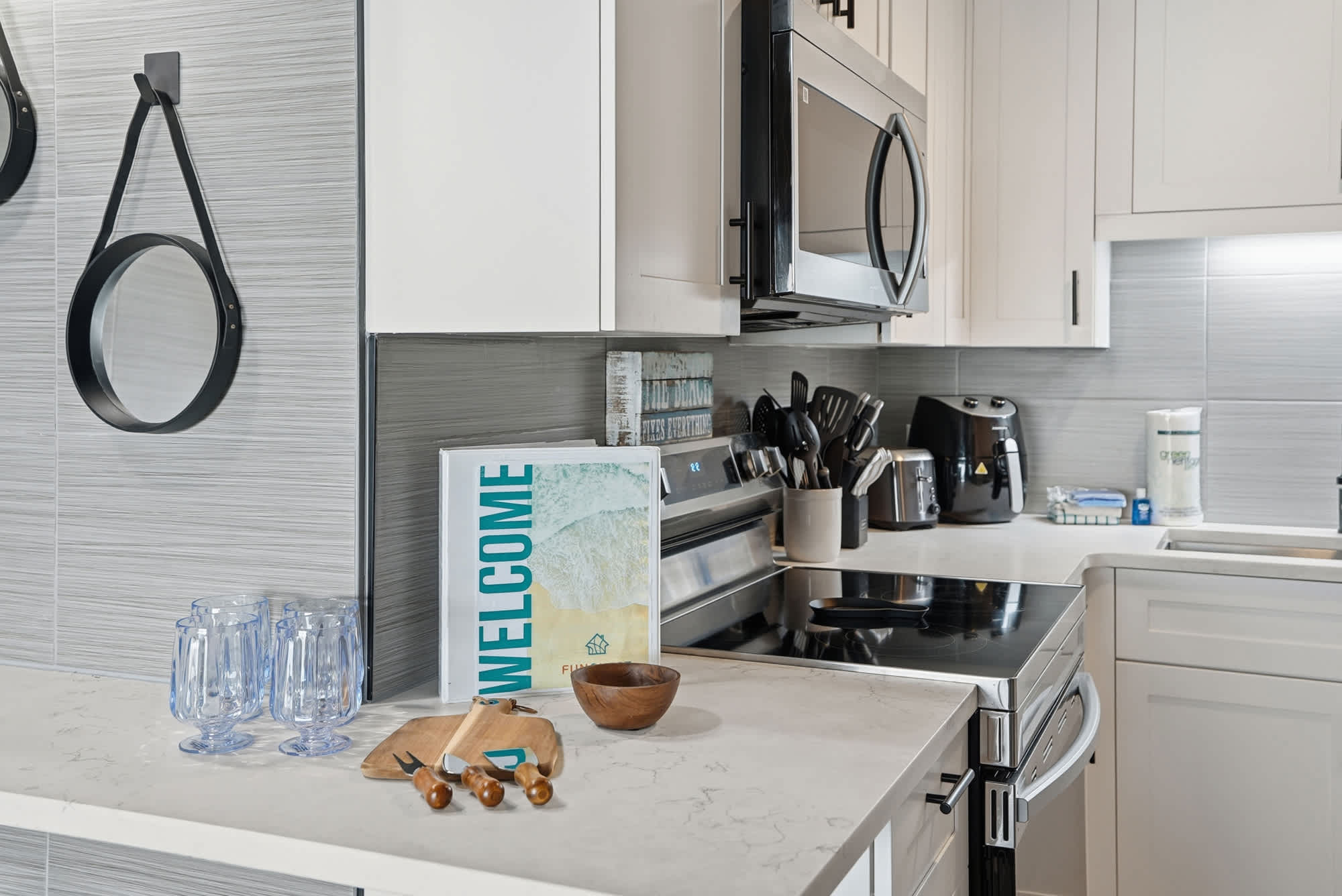 The Summit 1217 – Modern kitchen with white cabinets, stainless steel appliances, and marble countertops. Includes glassware and cooking utensils.