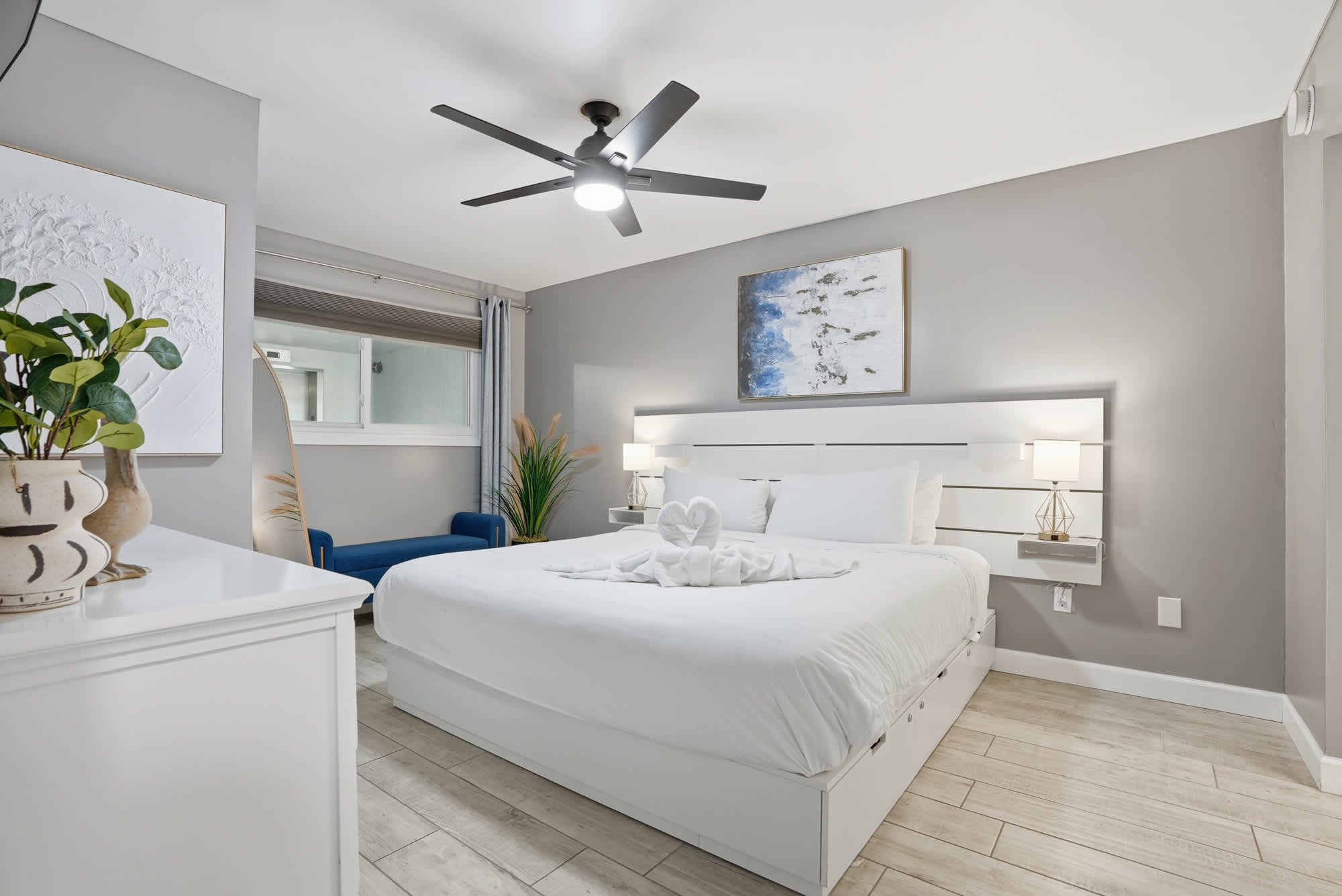 The Summit 1217 – Modern bedroom with a king-sized bed, nightstand, blue chair, and window view.
