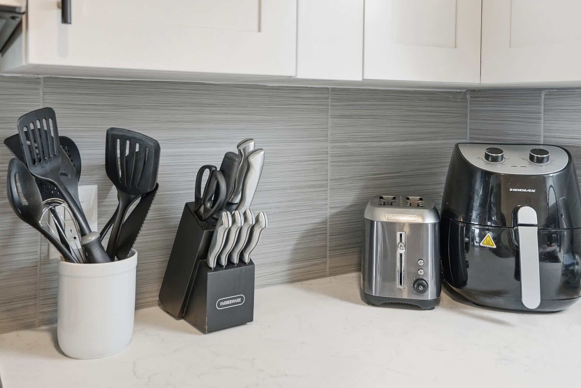 The Summit 1217 – Kitchen countertop with cooking utensils, knife block, toaster, and air fryer against a modern backsplash.