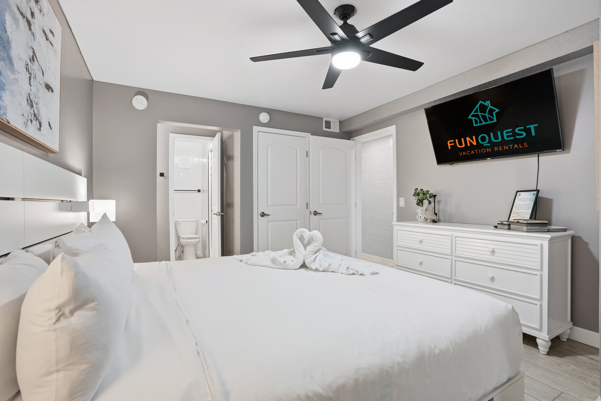 The Summit 1217 – Cozy bedroom with a king bed, ceiling fan, en-suite bathroom, and TV on the wall.