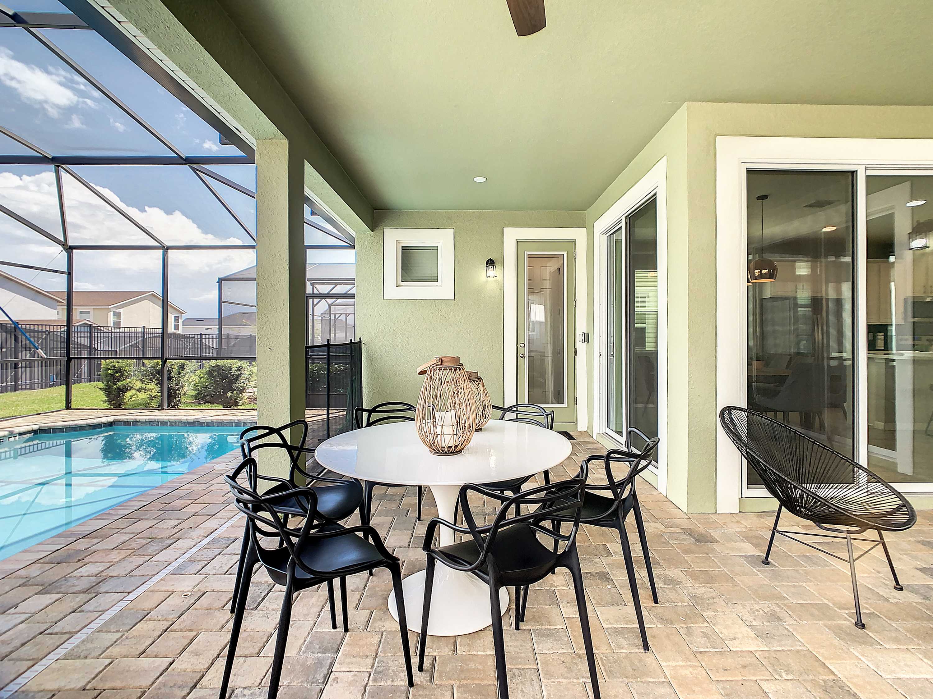 Covered poolside patio with a large outdoor dining table, seating for group meals, and sunny views through the screened enclosure.