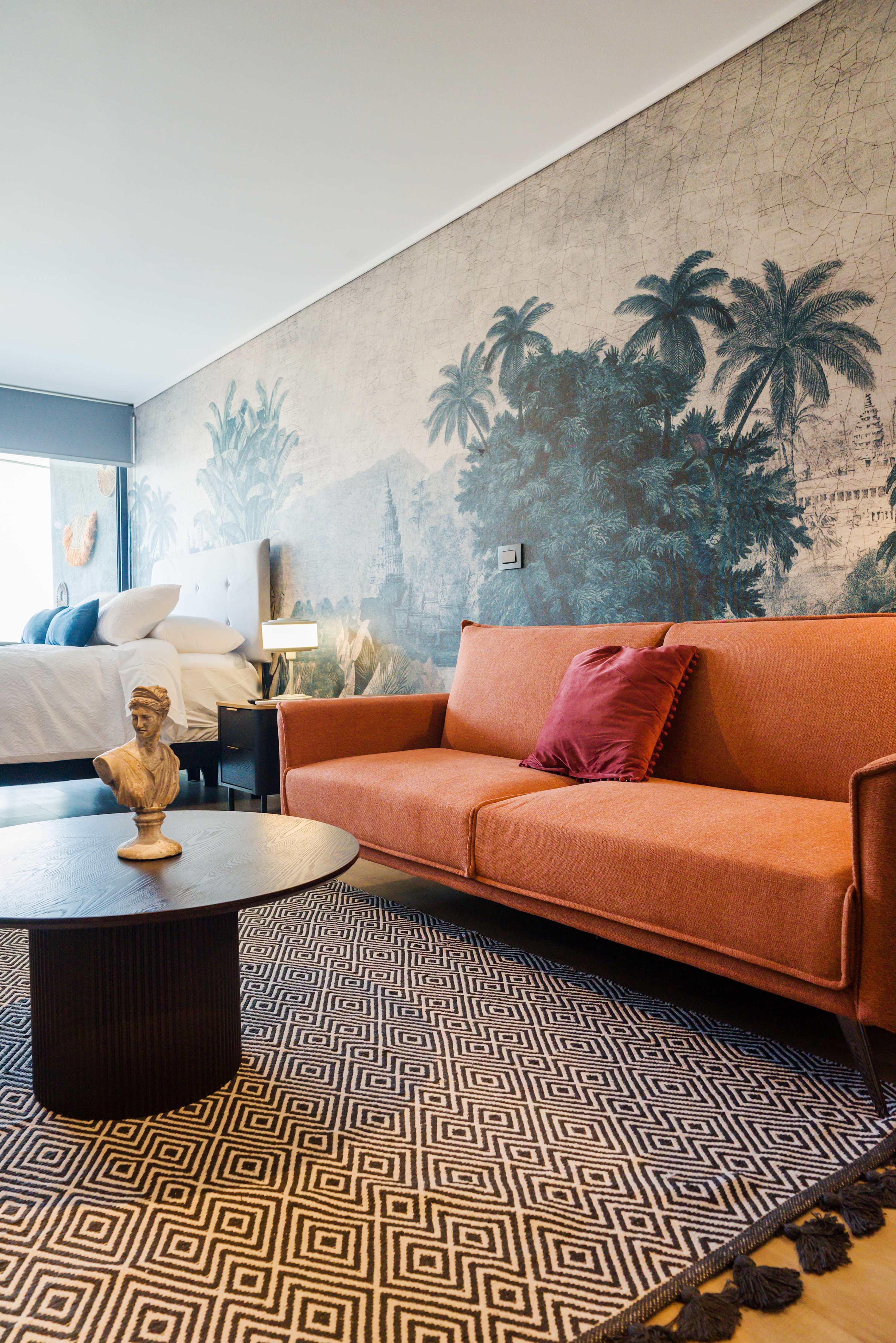 Experience a cozy retreat with a vibrant sofa and stunning mural backdrop in this stylish studio apartment.