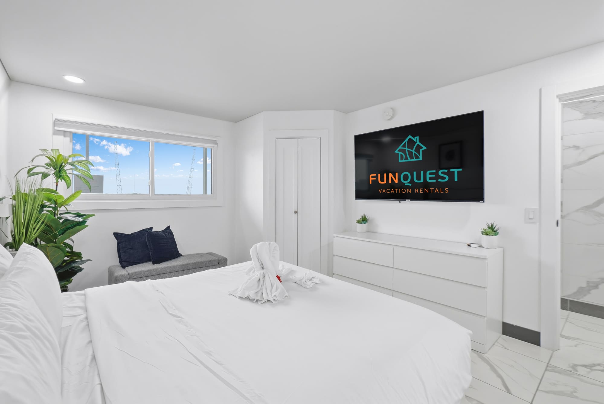 The Summit 1208 – Bright bedroom with a white bed, television, seating area, and window showing clear blue skies.
