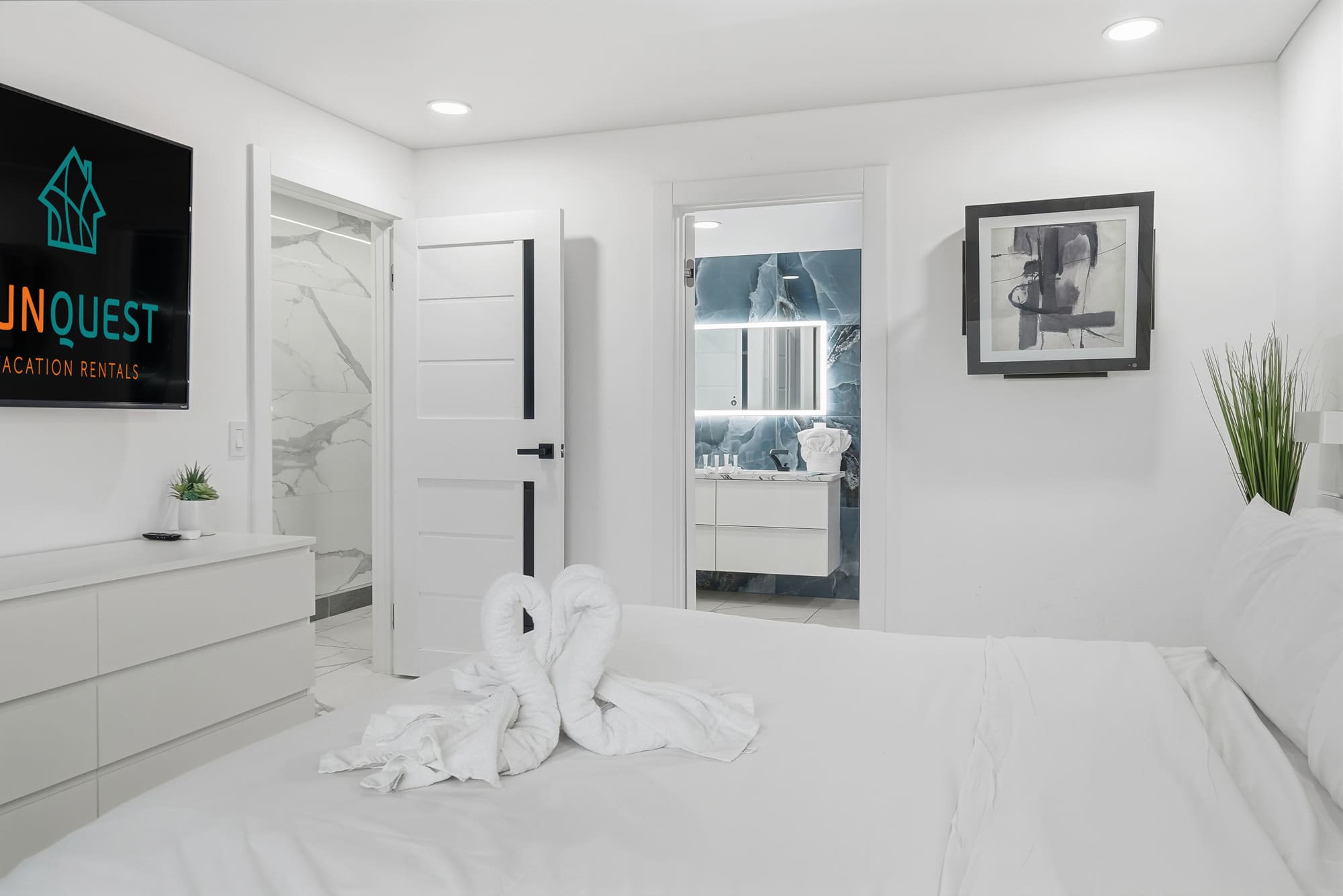 The Summit 1208 – Bedroom with a white bed, TV, and bathroom entrance featuring modern decor.