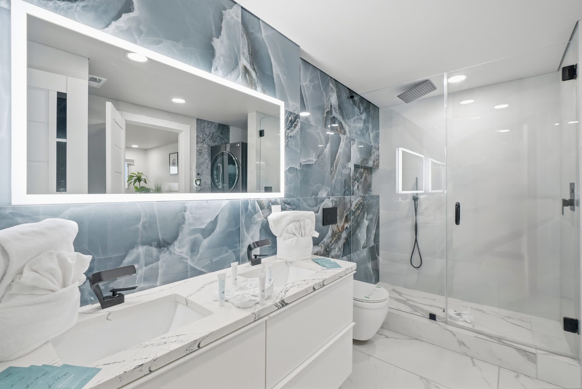 The Summit 1208 – Modern bathroom featuring a double sink, marble tiles, glass shower, and blue stone accent wall.