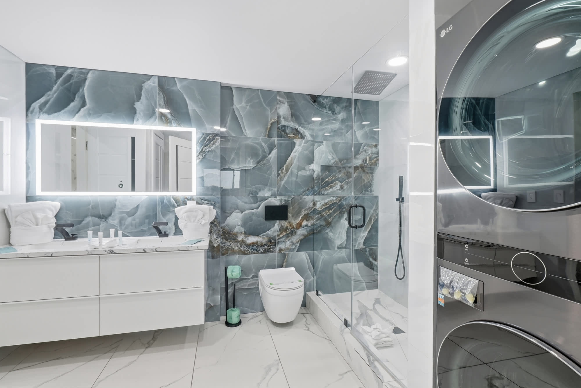 The Summit 1208 – Modern bathroom with stone walls, double vanity, walk-in shower, and washer-dryer unit.