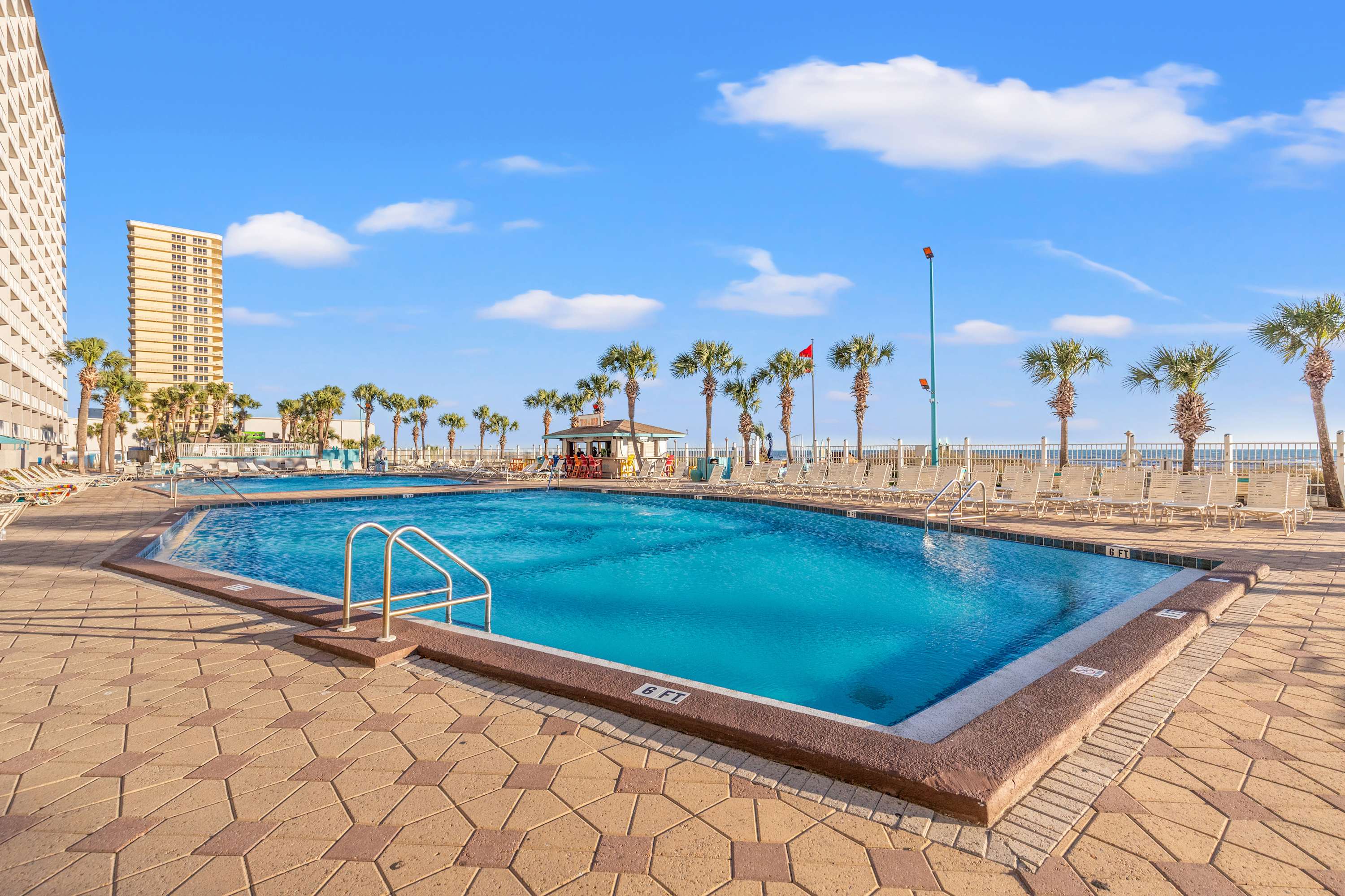 The Summit 1208 – Swimming pool area with palm trees and lounge chairs, ocean view in the background.