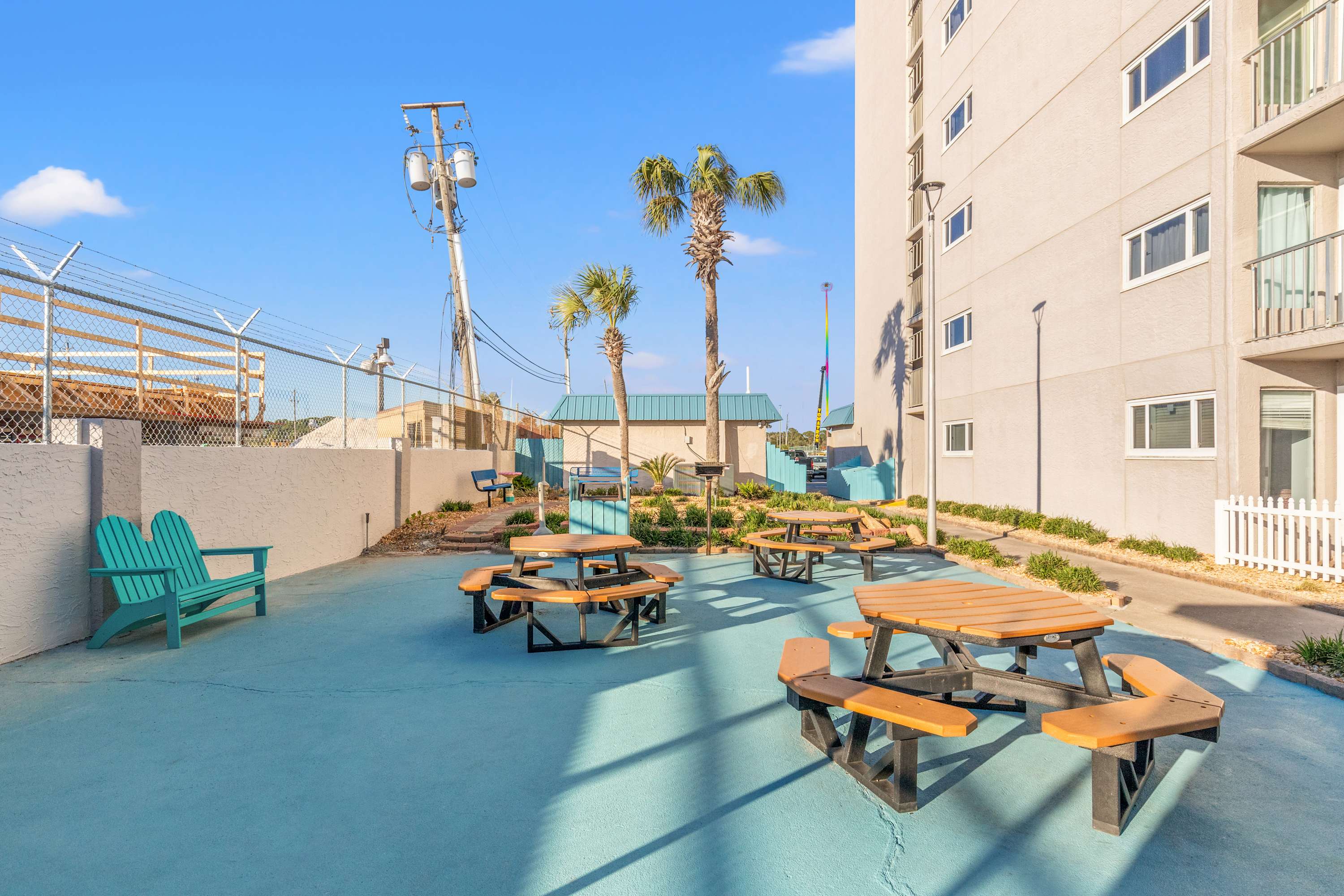 The Summit 1208 – Outdoor seating area with picnic tables, palm trees, and a view of a neighboring building.