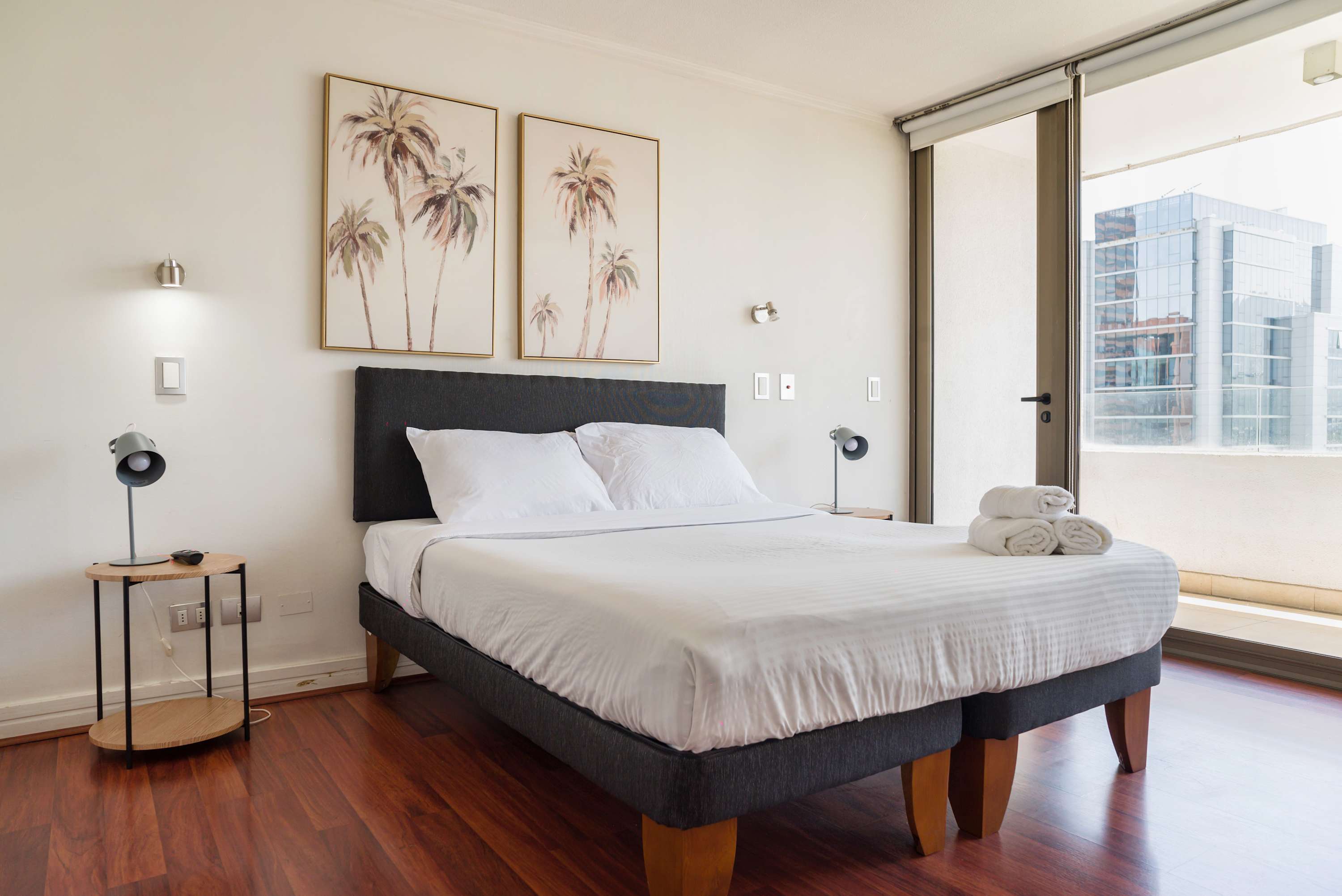 Relax in this bright and airy bedroom with city views, featuring modern decor and cozy bedding.
