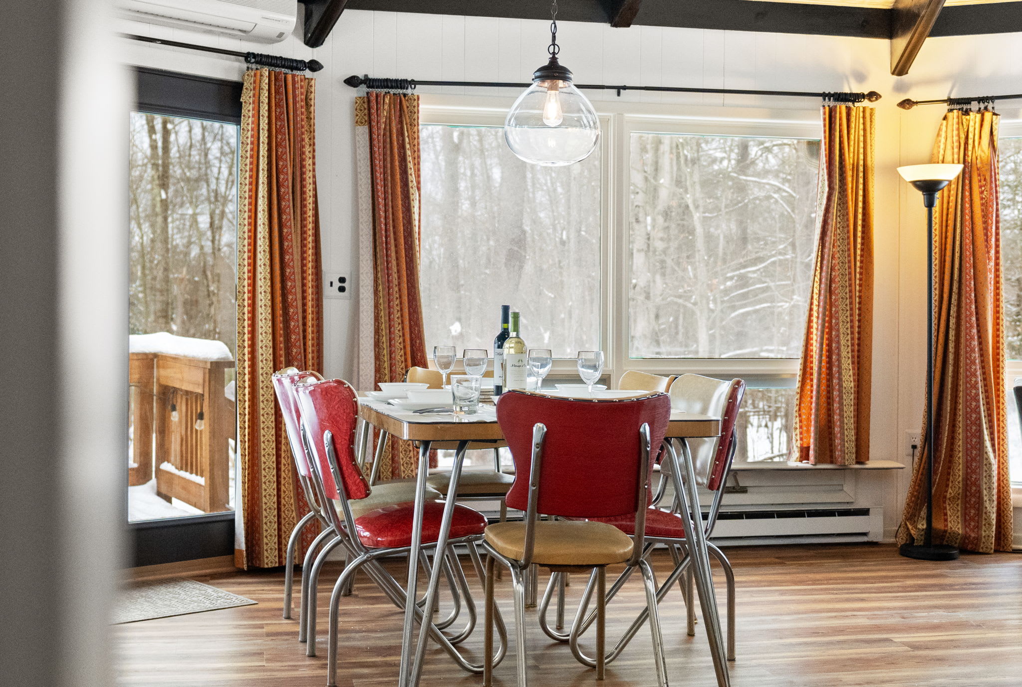 Rustic dining area with vintage red chairs and panoramic window views in Pocono Mountains cabin