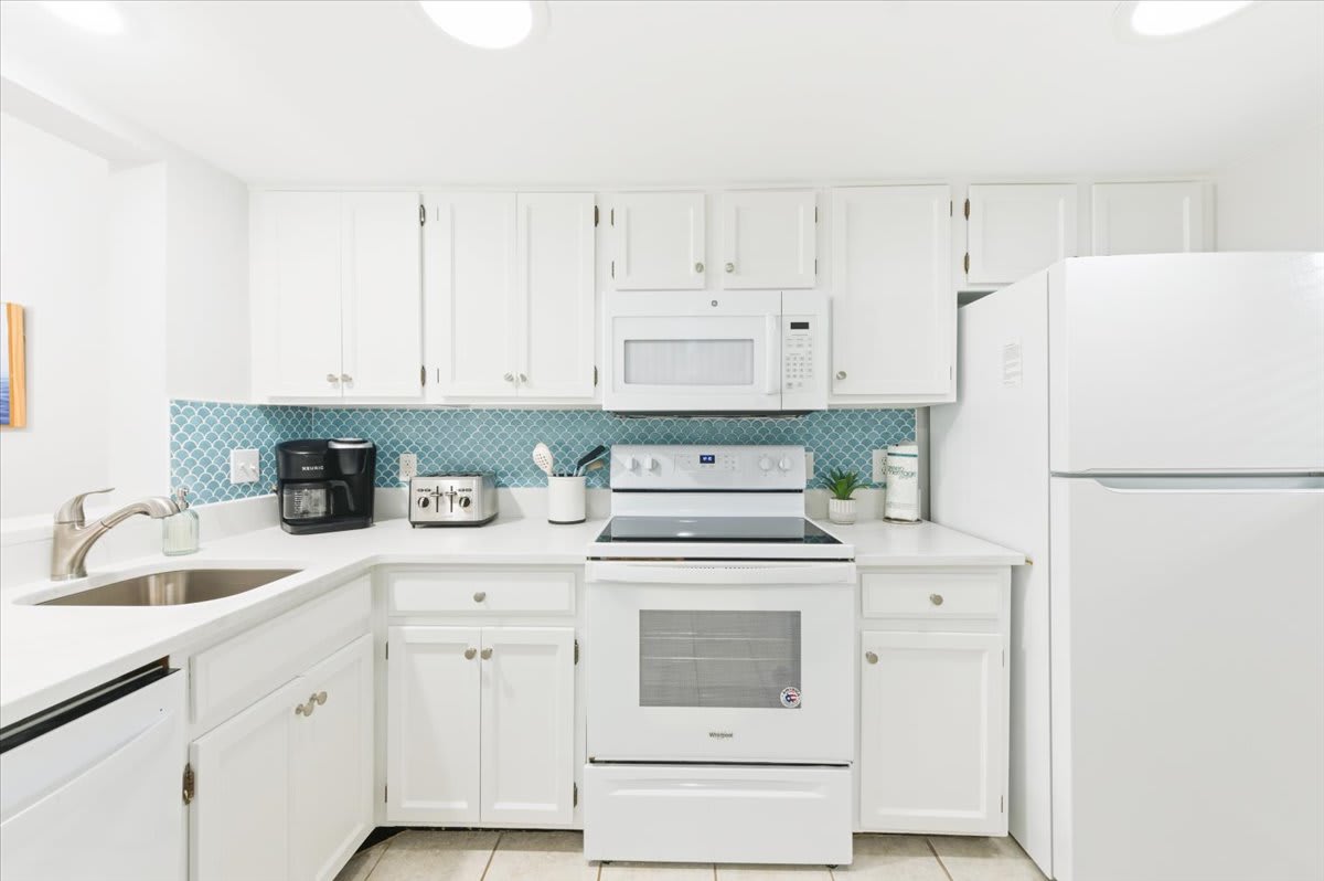 Bright, coastal kitchen with full-size appliances, coffee maker, and blue tile splash.